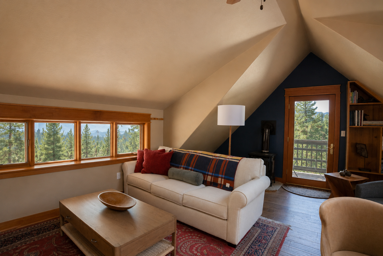 Cozy living room with a cream sofa, throw pillows, wooden coffee table, and large windows with forest view, under a sloped ceiling with a sky blue wall and small balcony door.