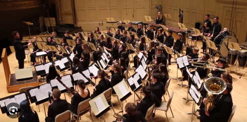 Large orchestra of musicians playing instruments in a concert hall.
