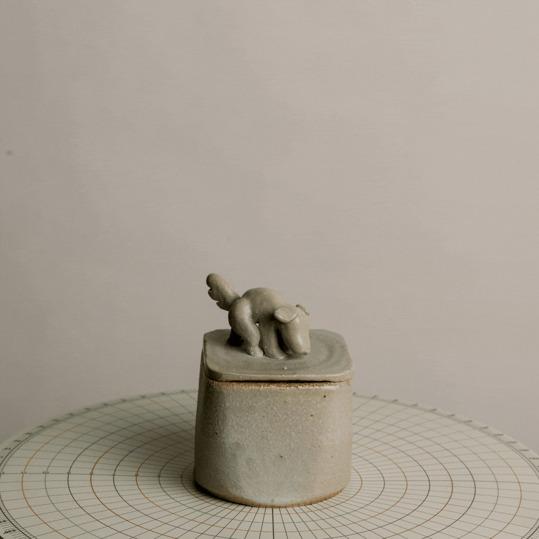 A small grey sculpture of an elephant with a smaller elephant riding on its back, placed on a round, grey pedestal on a circular, grid-patterned surface.
