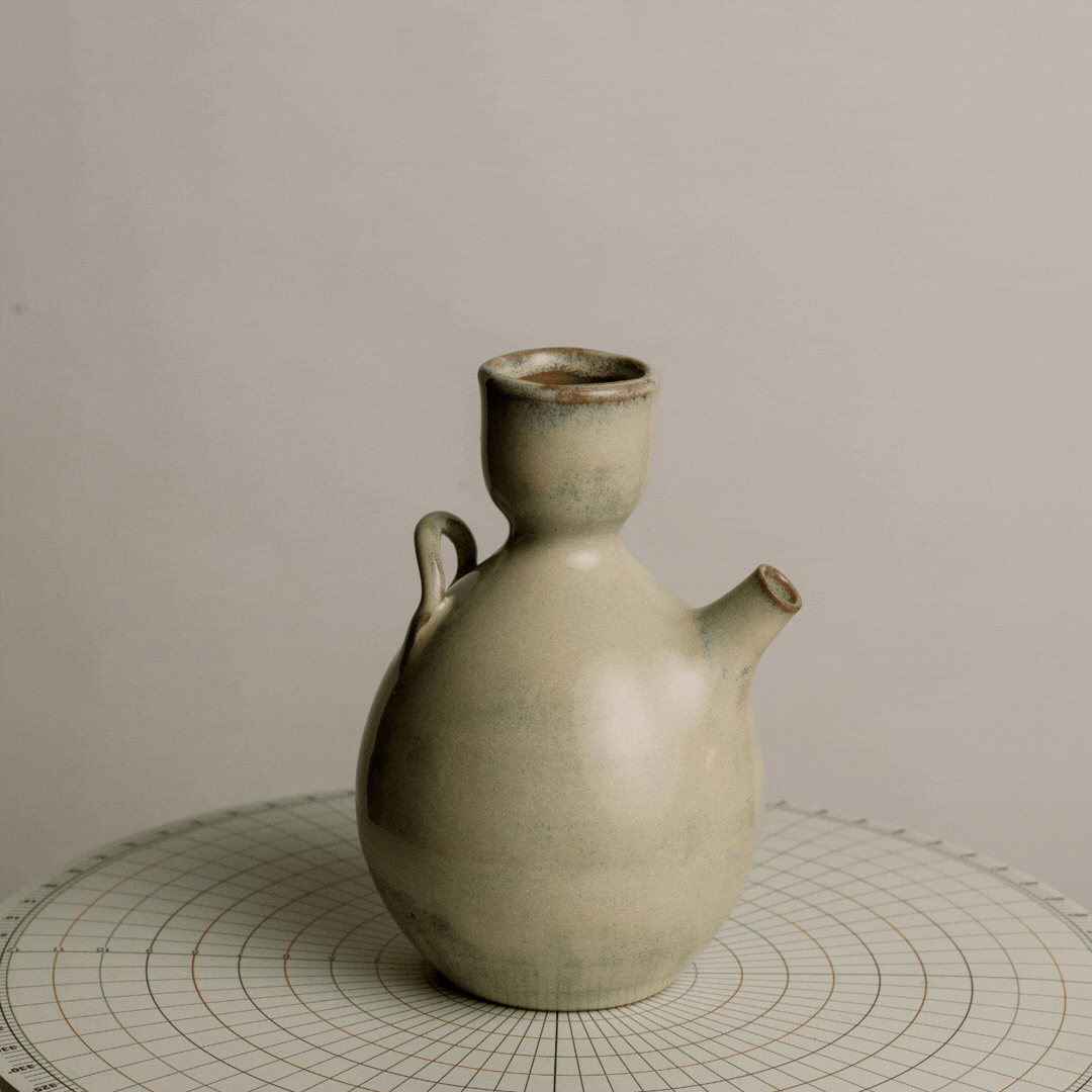 Ceramic teapot with a round body, short spout, and small handle, placed on a circular grid surface against a light background.