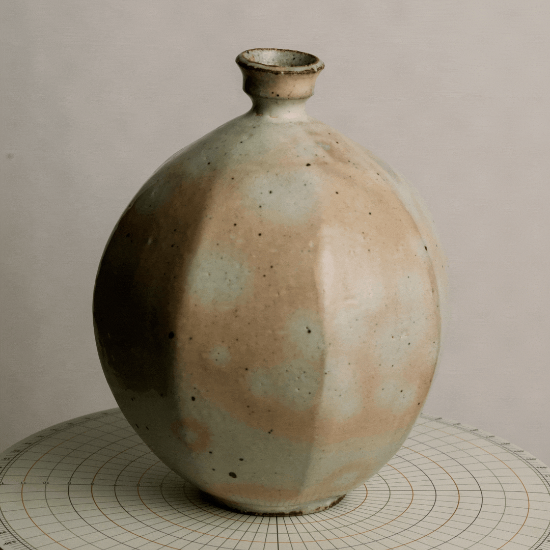 A ceramic vase with a rounded body, short neck, and narrow opening, resting on a circular grid-patterned surface.
