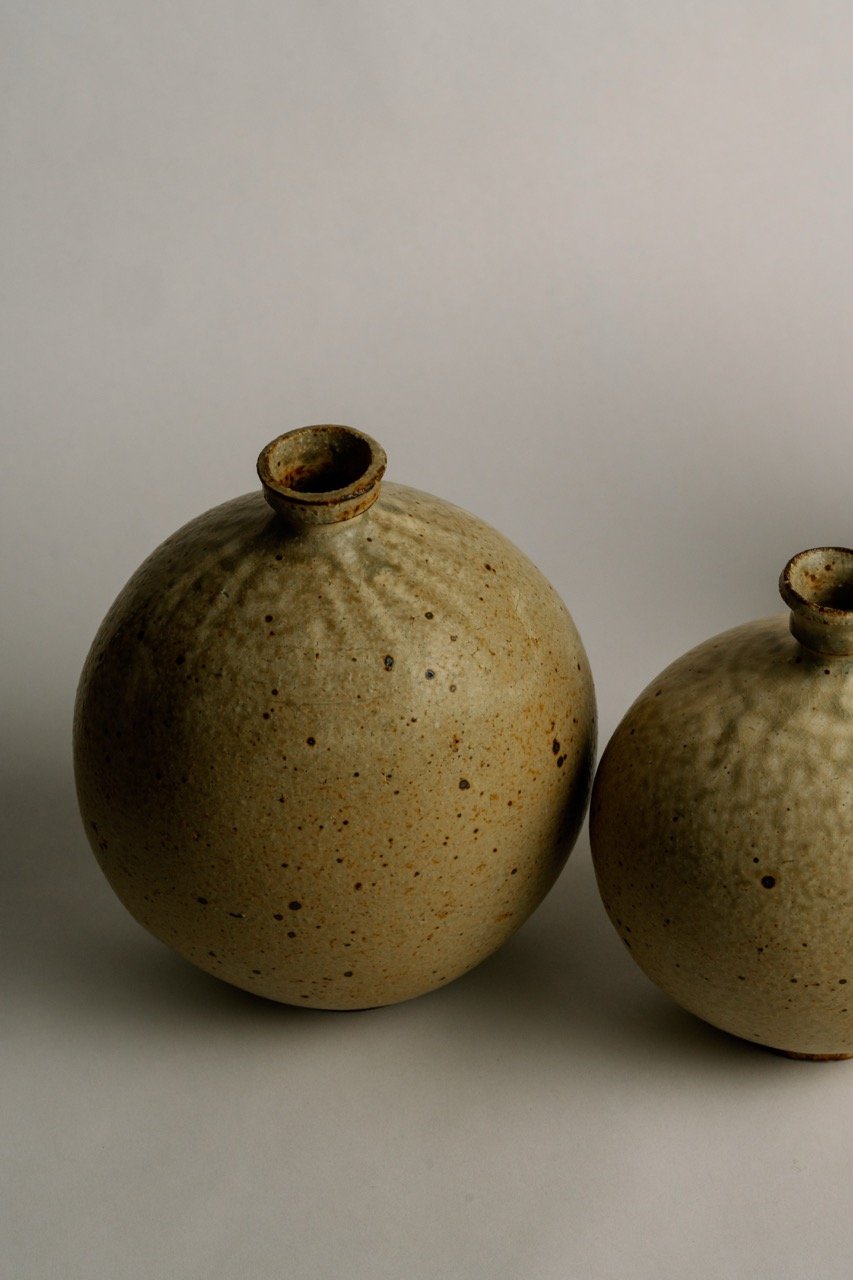 Two beige ceramic vases with narrow openings, placed on a plain surface against a light background.