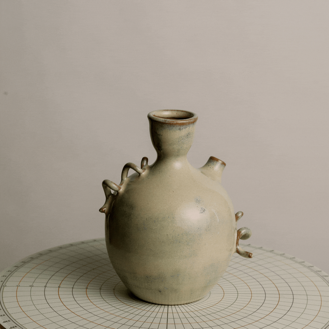 Ceramic vase with multiple small sculptural appendages, placed on a circular grid paper