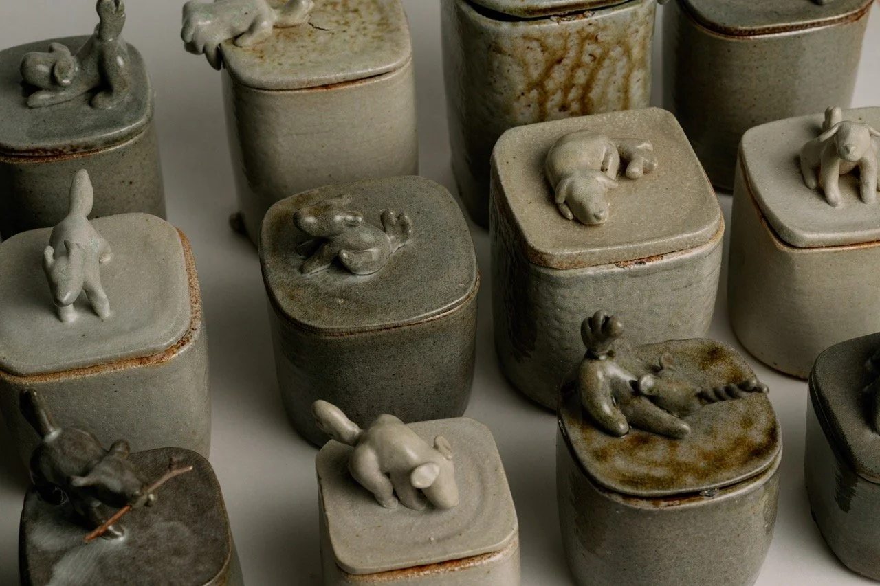 Collection of small ceramic containers with animal-shaped toppers, including rabbits, unicorns, and other creatures, arranged on a flat surface.