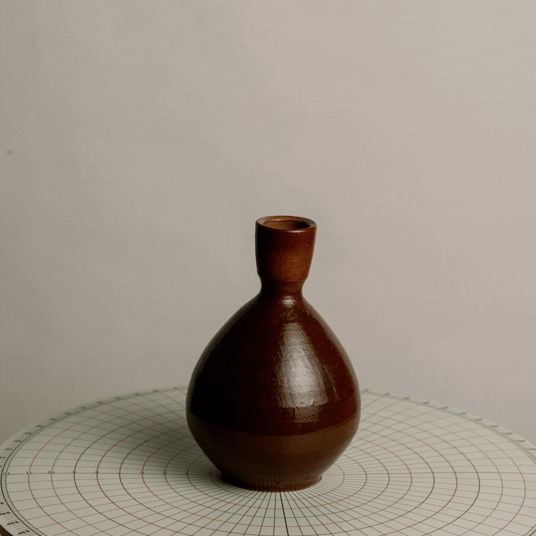 A brown ceramic vase with a round base and narrow neck on a circular cutting mat.