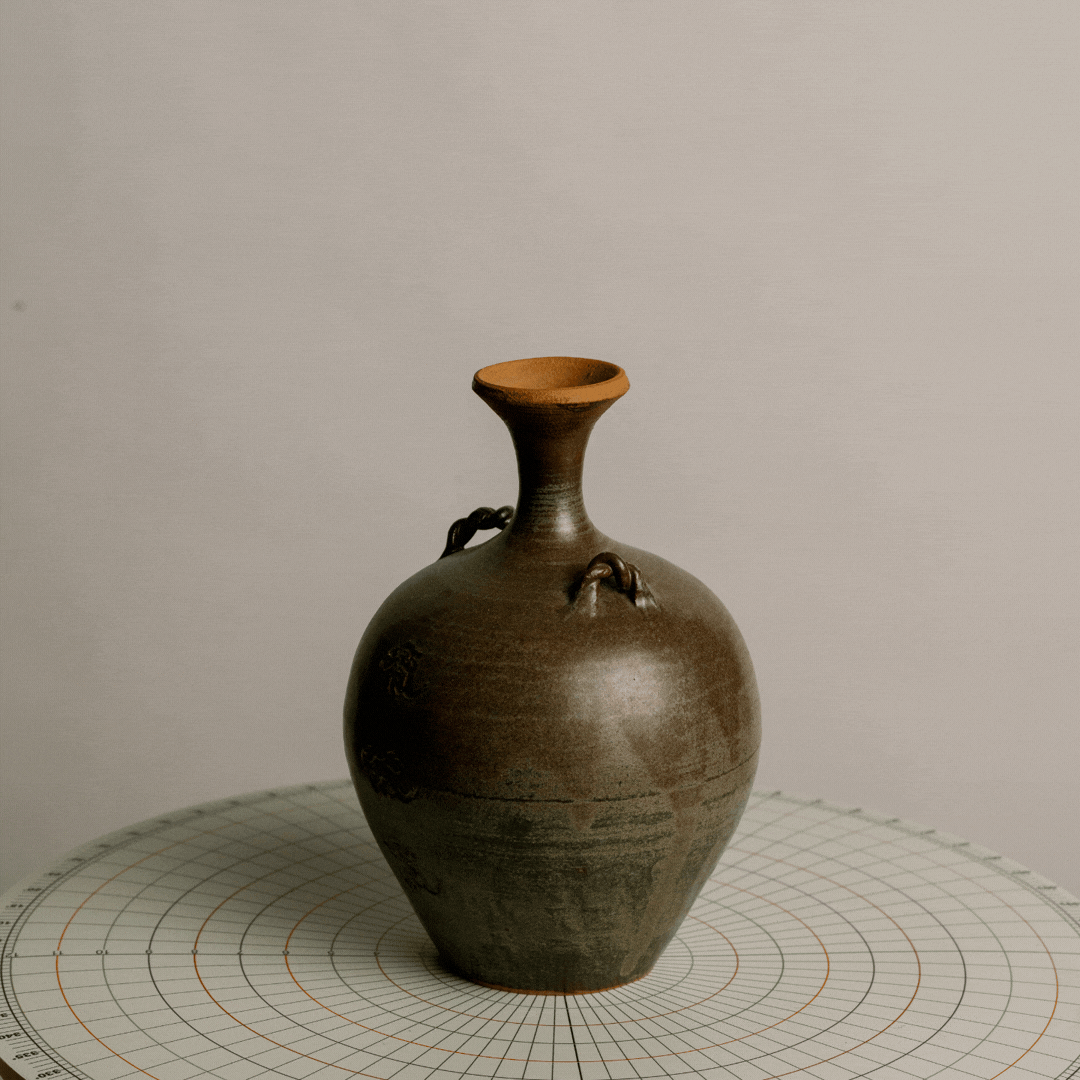 An ancient ceramic vase with a narrow neck and two decorative handles, placed on a circular grid surface.