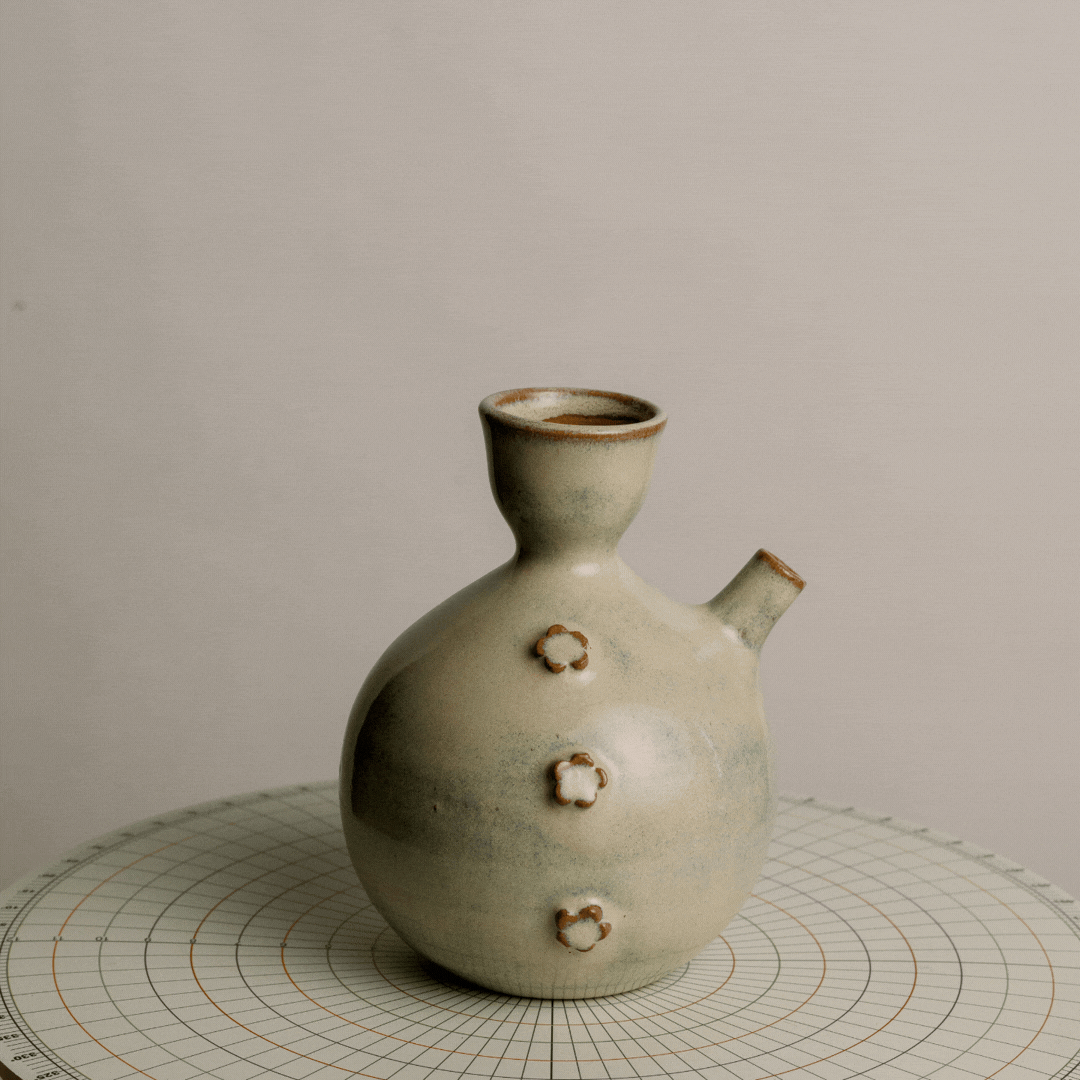 Ceramic vase with flower-shaped decorations on a textured surface, against a plain background.
