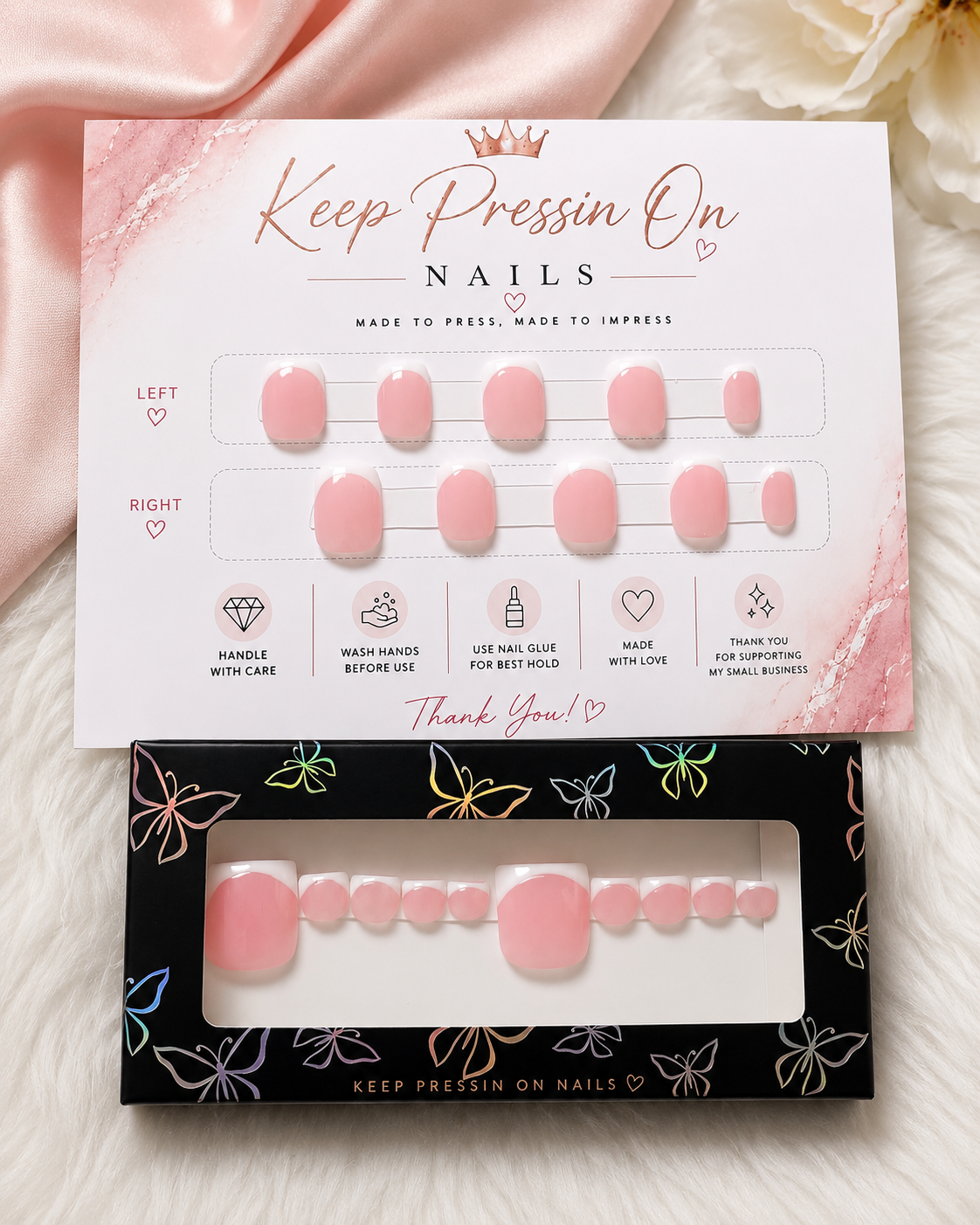 Pink press-on nail sets on decorative display board with instructions, placed on a soft white surface with pink and white fabrics nearby.