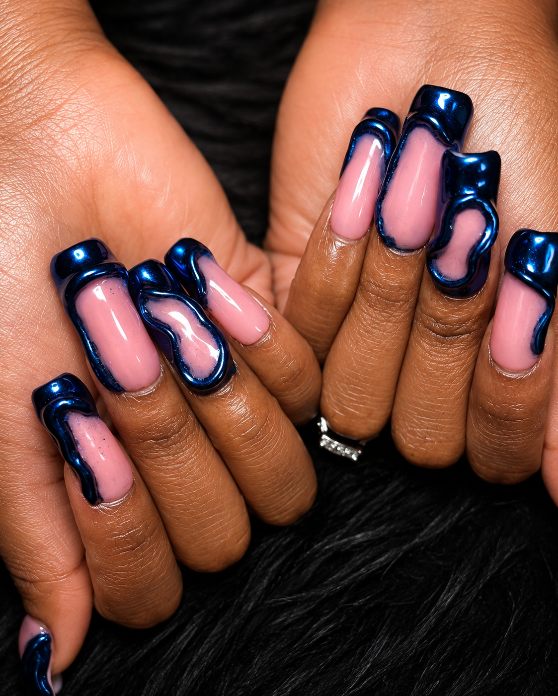 Close-up of a person's hands with pink nail polish and curly, dark blue, glossy, 3D-style nail art.