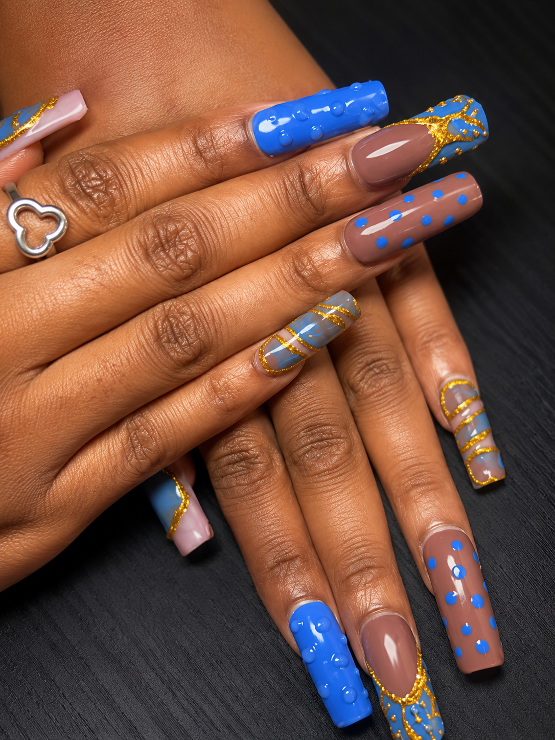 Close-up of hands with decorated long acrylic nails in blue, pink, and clear polish with gold accents and polka dots.