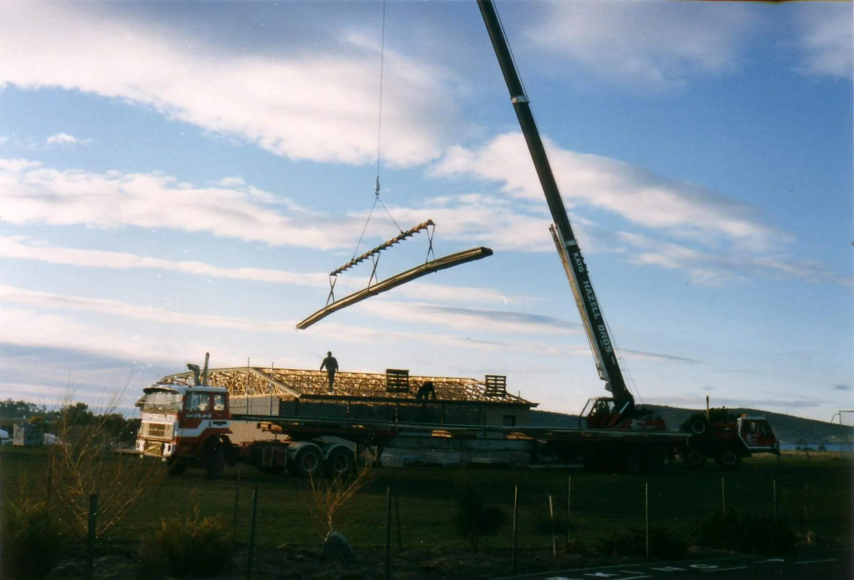 An historic colour image of a crane putting the roof on a school