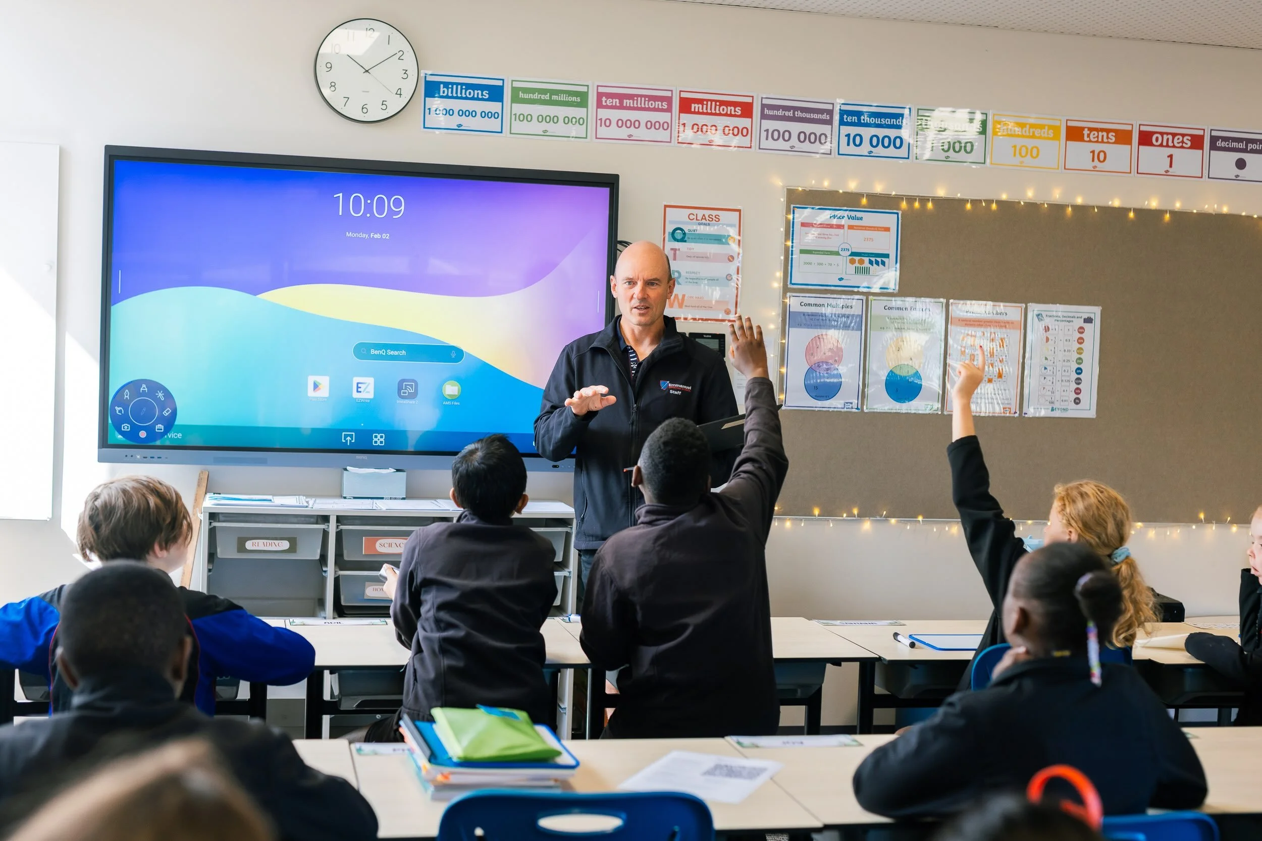 Primary students raise their hands to answer a question from the teacher in a classroom at Emmanuel Christian School in Rokeby, Tasmania.