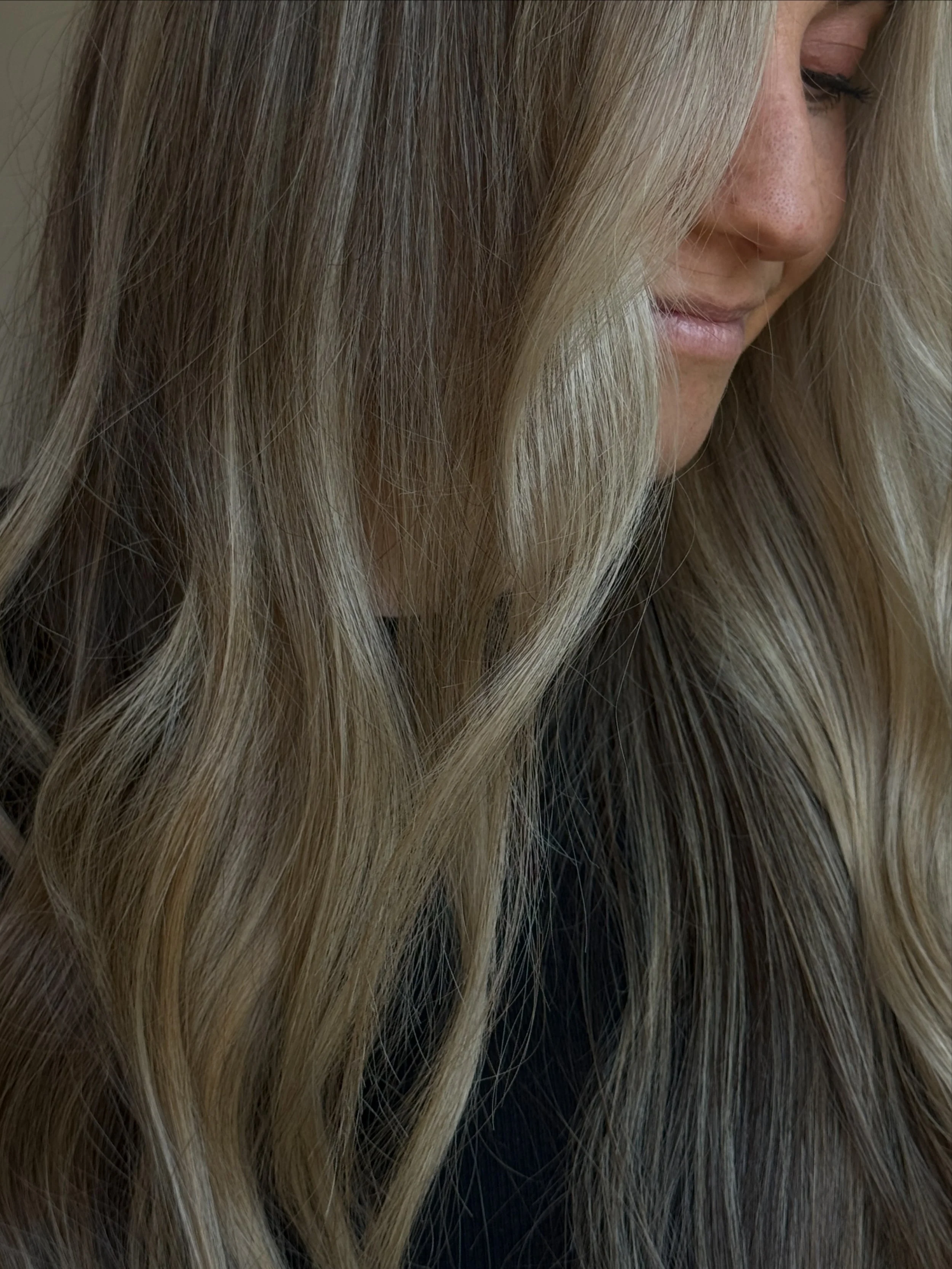 Close-up of a woman with long blonde hair covering part of her face, showing her nose, lips, and closed eyes.