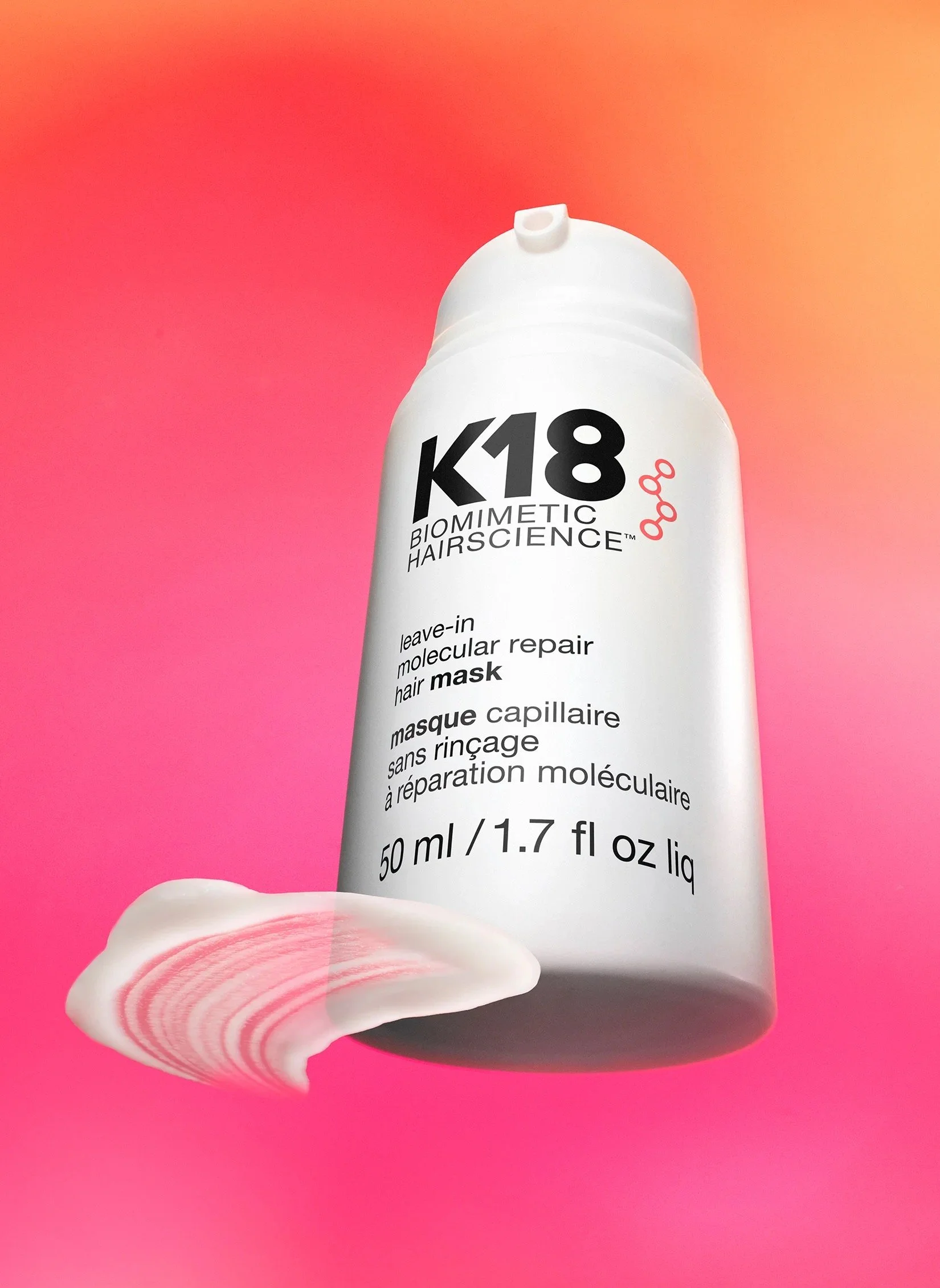 A white bottle of K18 Biometric Hairscience leave-in molecular repair hair mask with a pink and orange gradient background.