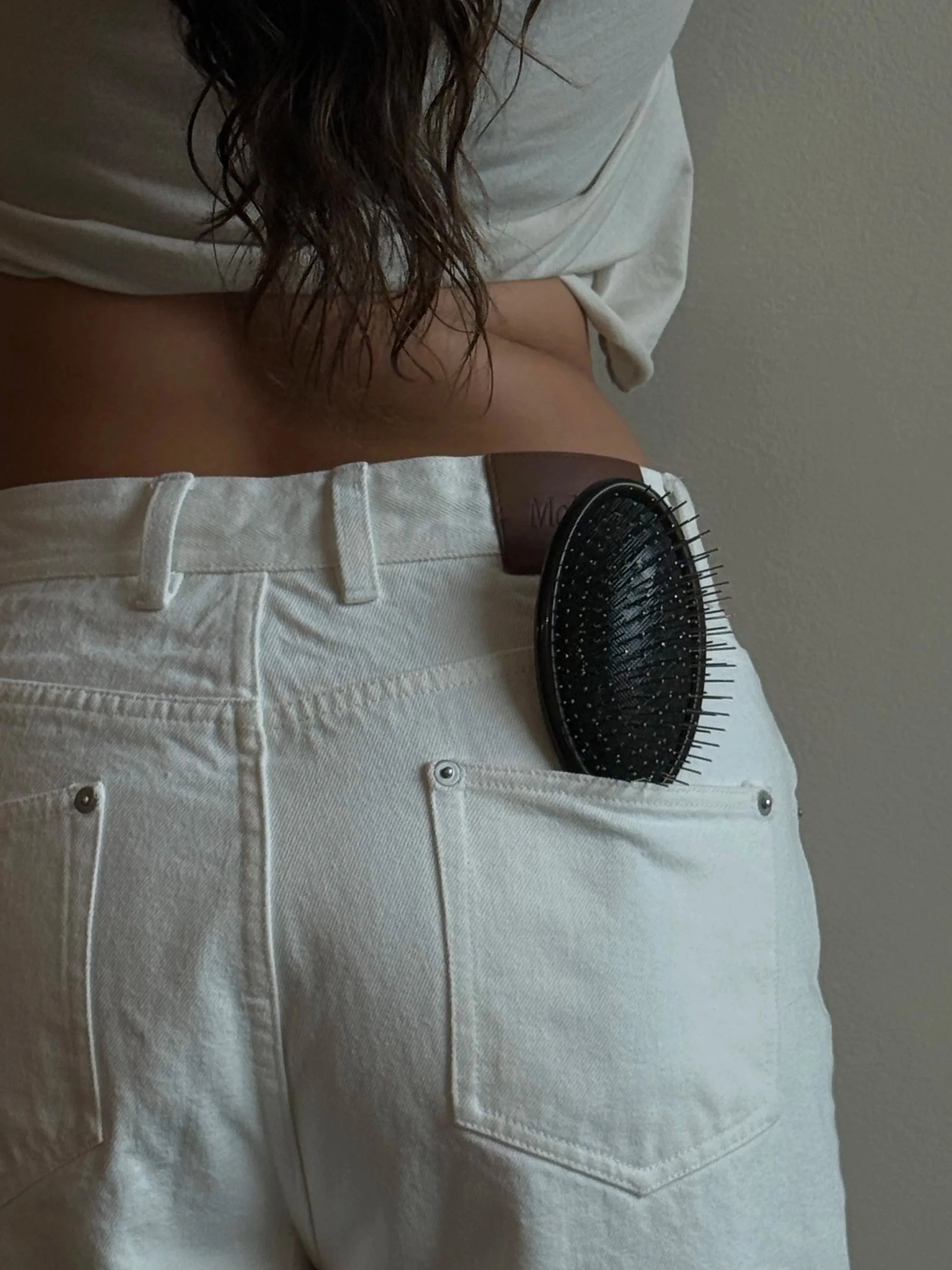 A person wearing white jeans with a brown hairbrush partially tucked into the back pocket.