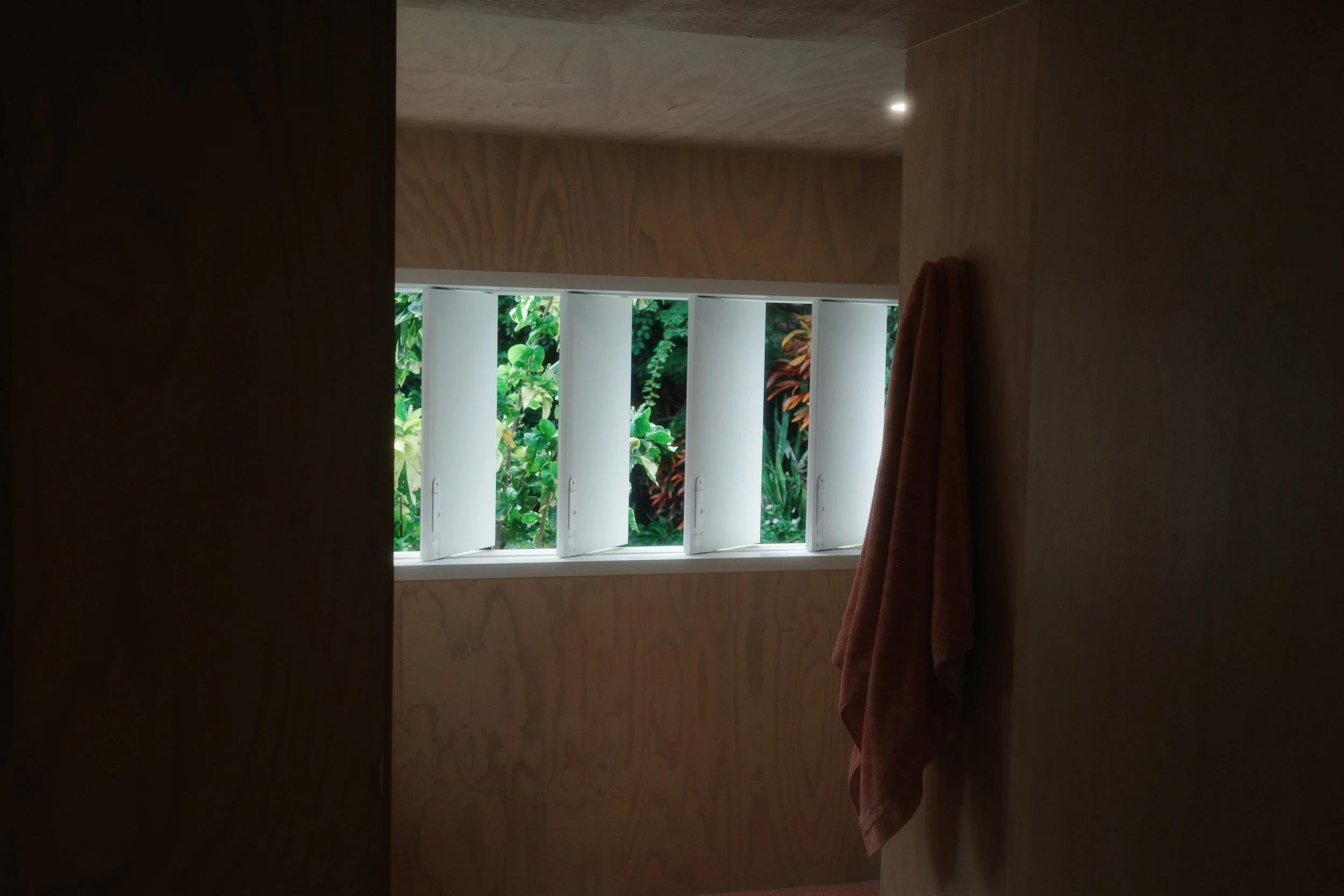 Plywood-lined room with vertical timber window slats and a towel hanging on the wall