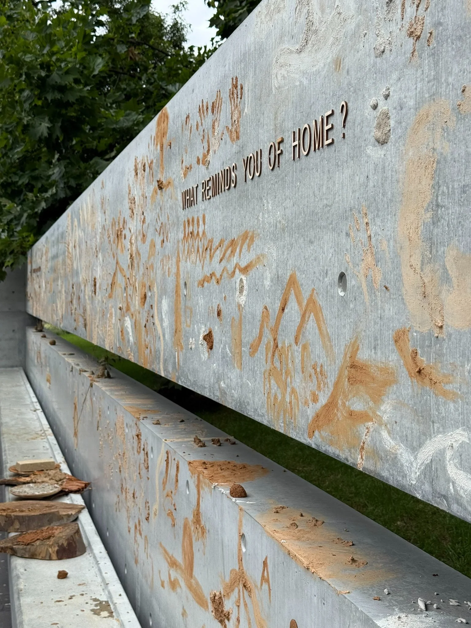 Long concrete wall covered in ochre marks and drawings, lettered with the question "What reminds you of home?"