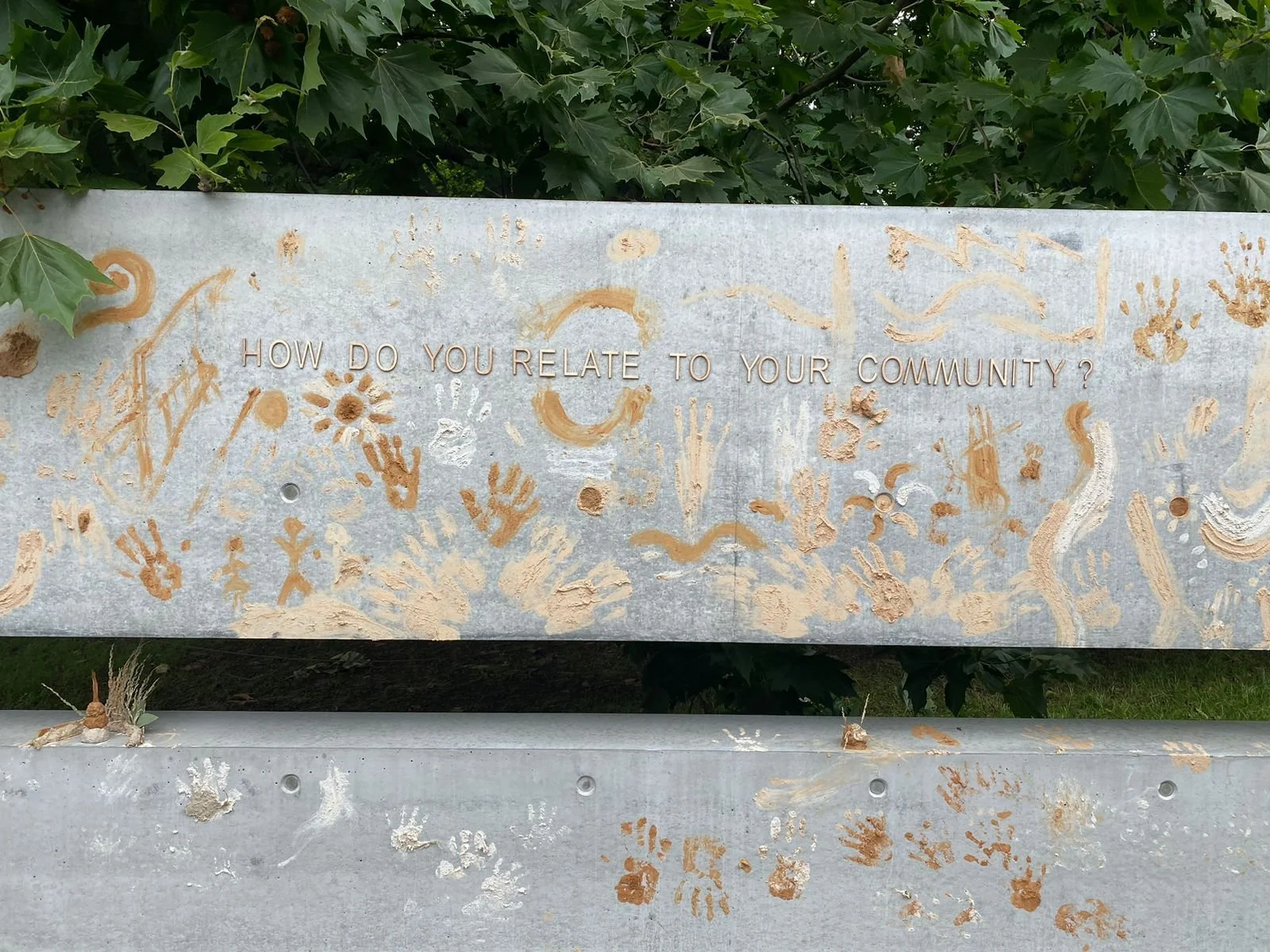 Concrete wall covered in ochre handprints and drawings beneath the lettered question "How do you relate to your community?"