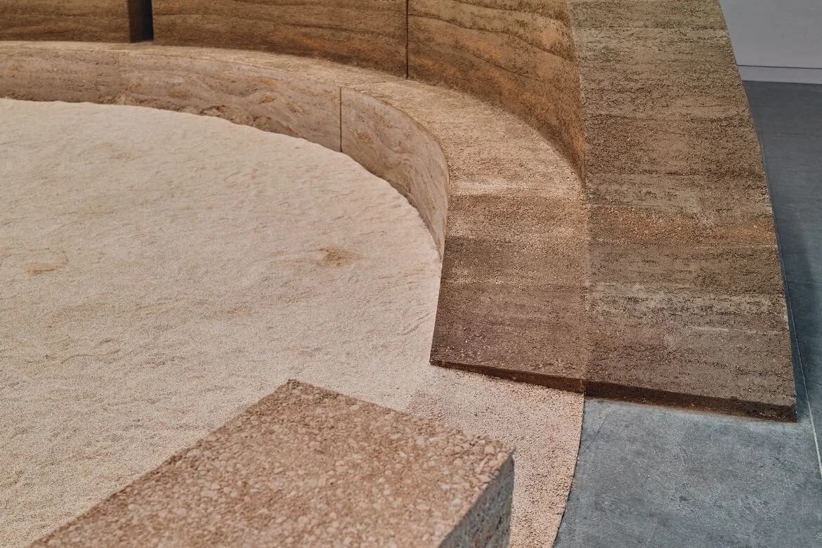 Sand-filled circle ringed by a curved rammed earth bench inside the HOME pavilion in Venice