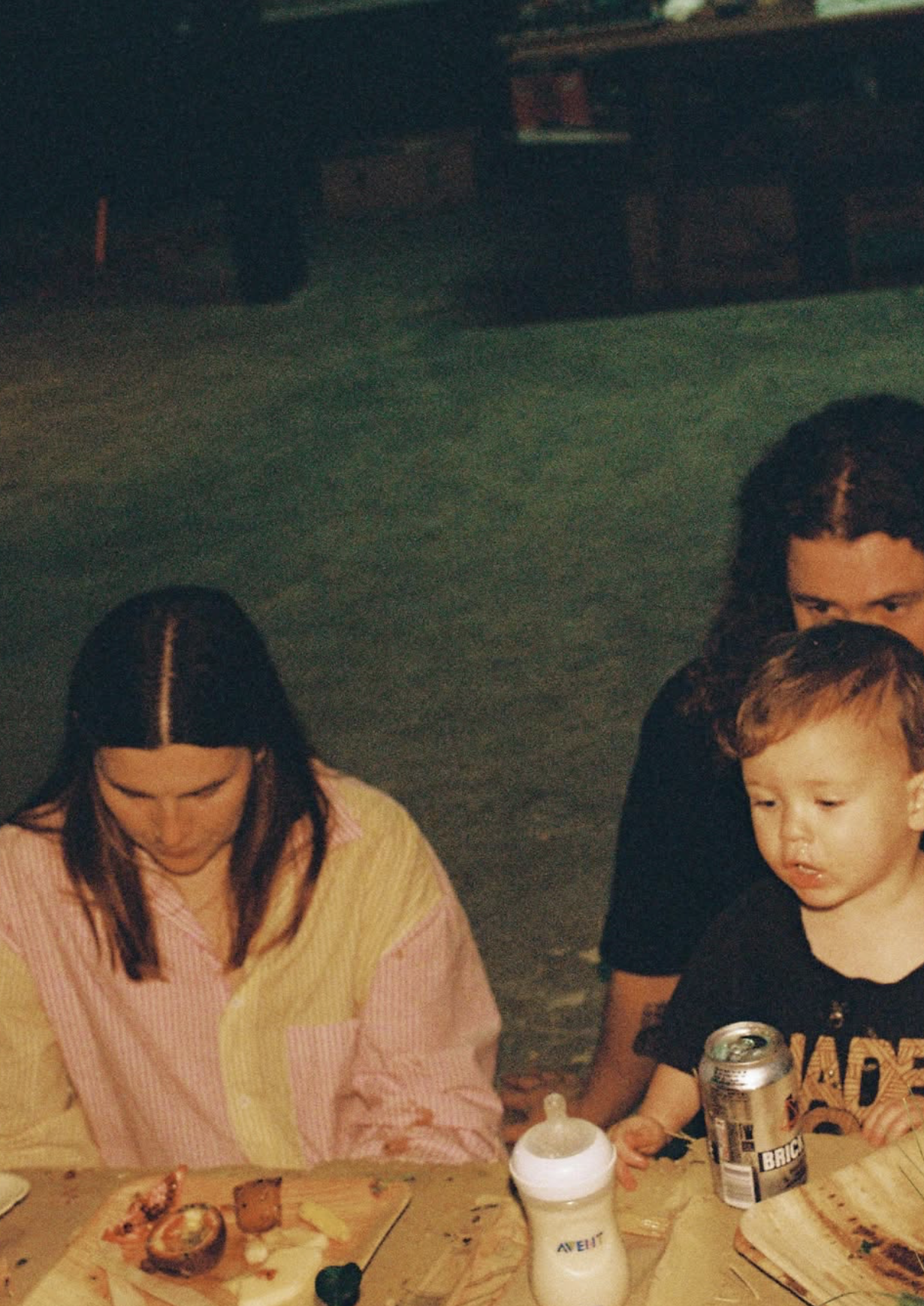 Guests sharing food at a table in the evening, a toddler among them