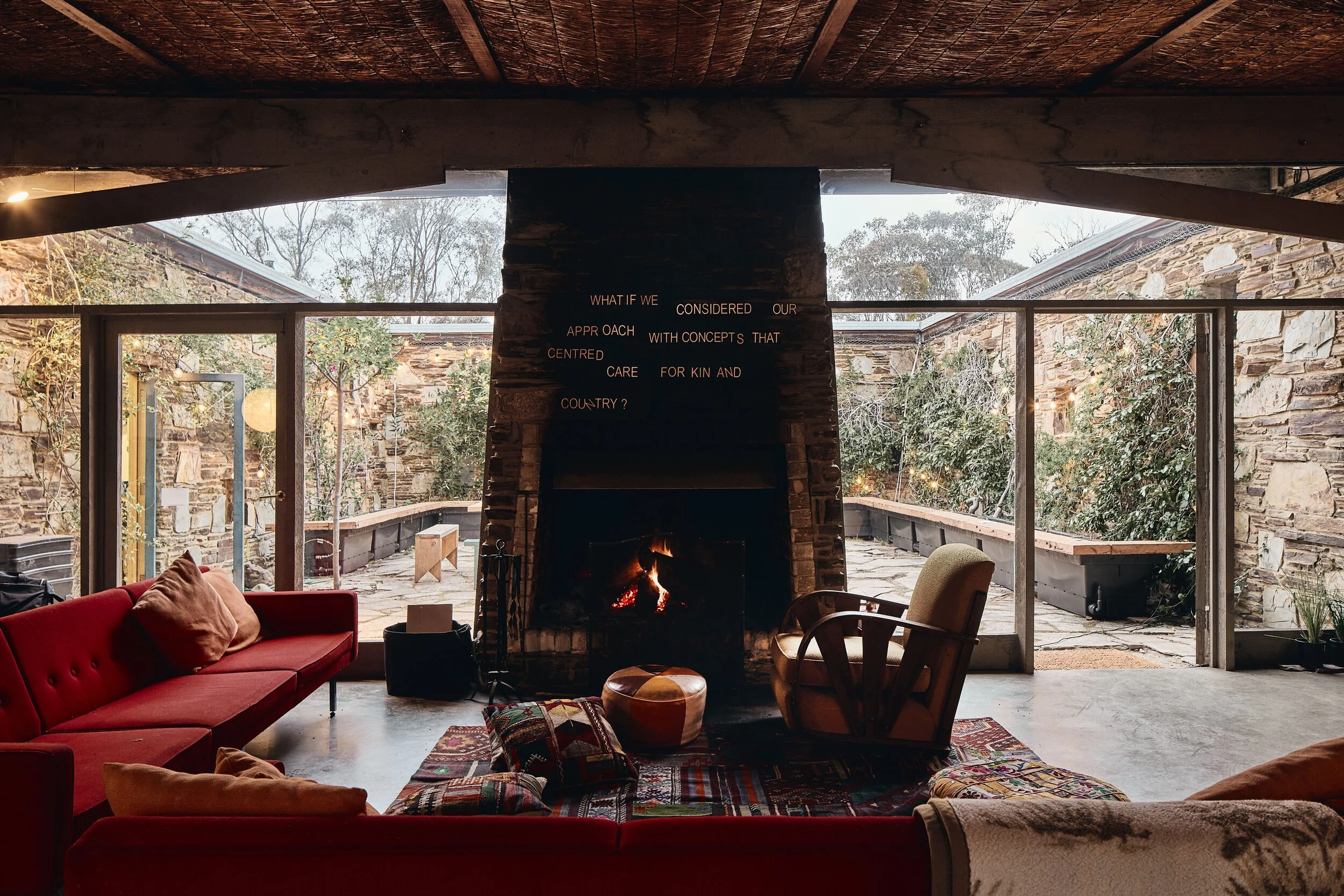 A New Normal at Boyd Baker House: living room with red sofas facing a stone fireplace lettered "What if we considered our approach with concepts that centred care for kin and Country?"
