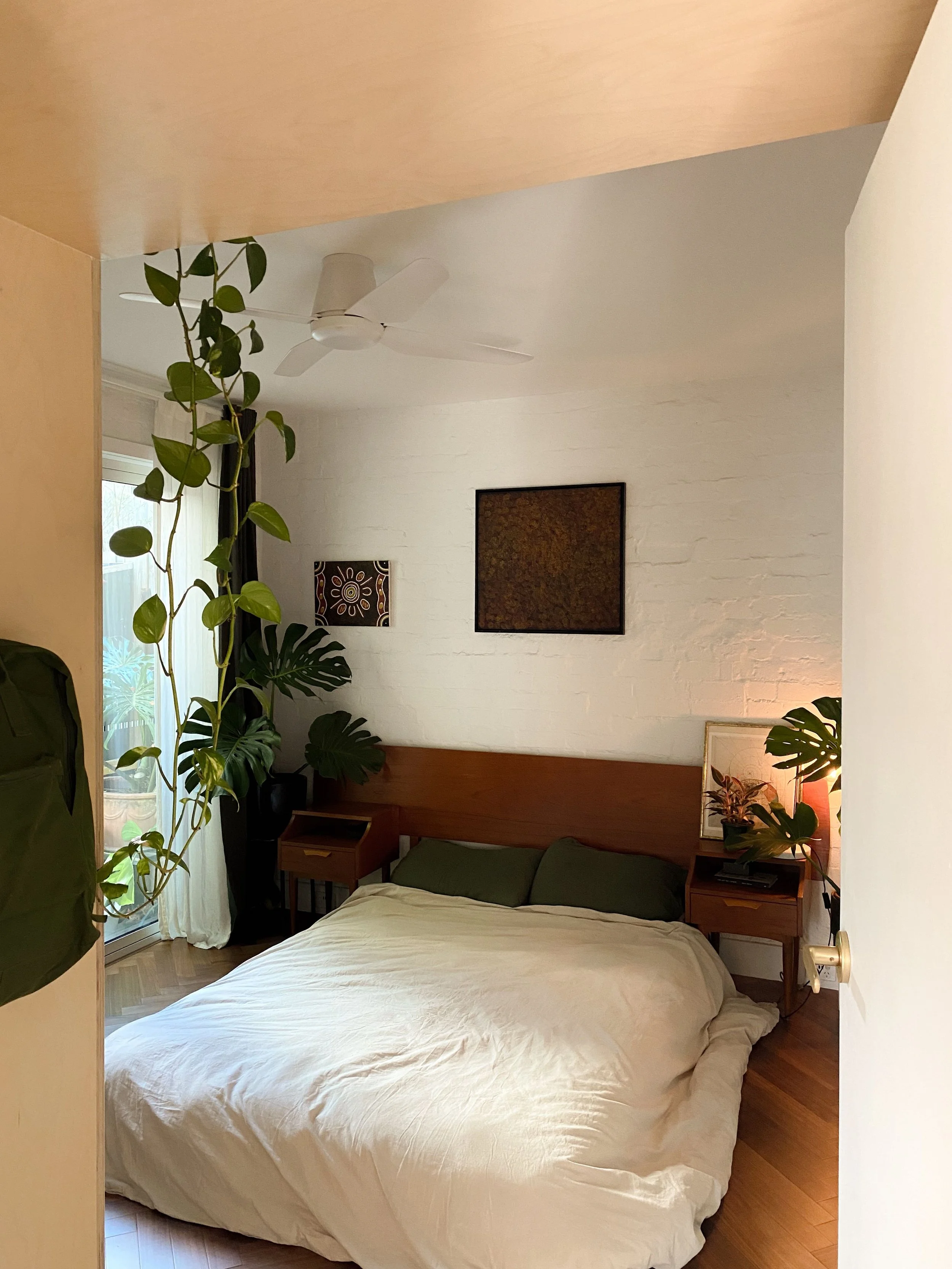 Manningham Street bedroom with painted white brick walls, a timber bedhead and trailing indoor plants