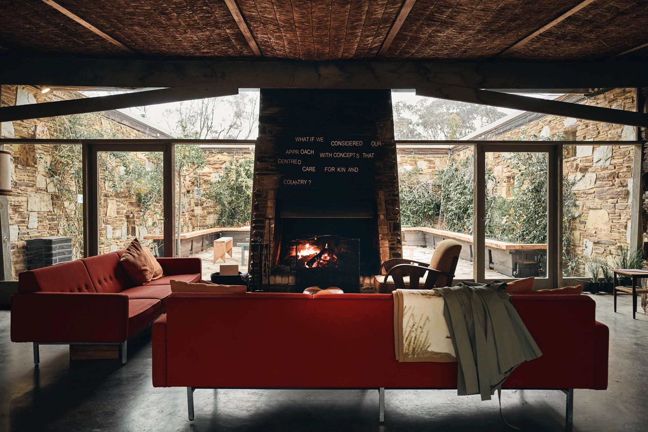 Living room with red sofas facing a stone fireplace lettered "What if we considered our approach with concepts that centred care for kin and Country?"