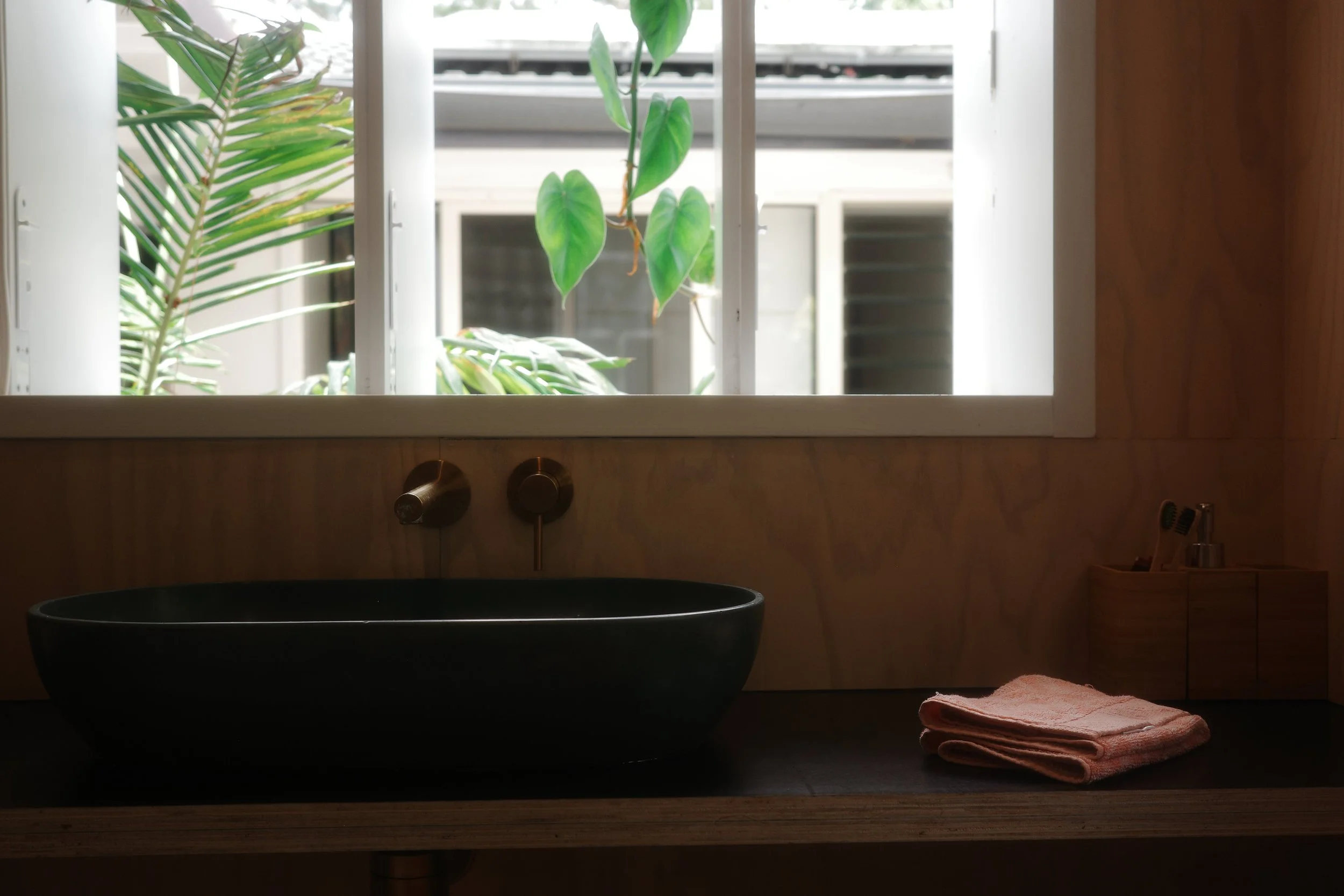 Dark stone basin on a timber vanity beneath a window looking out to greenery