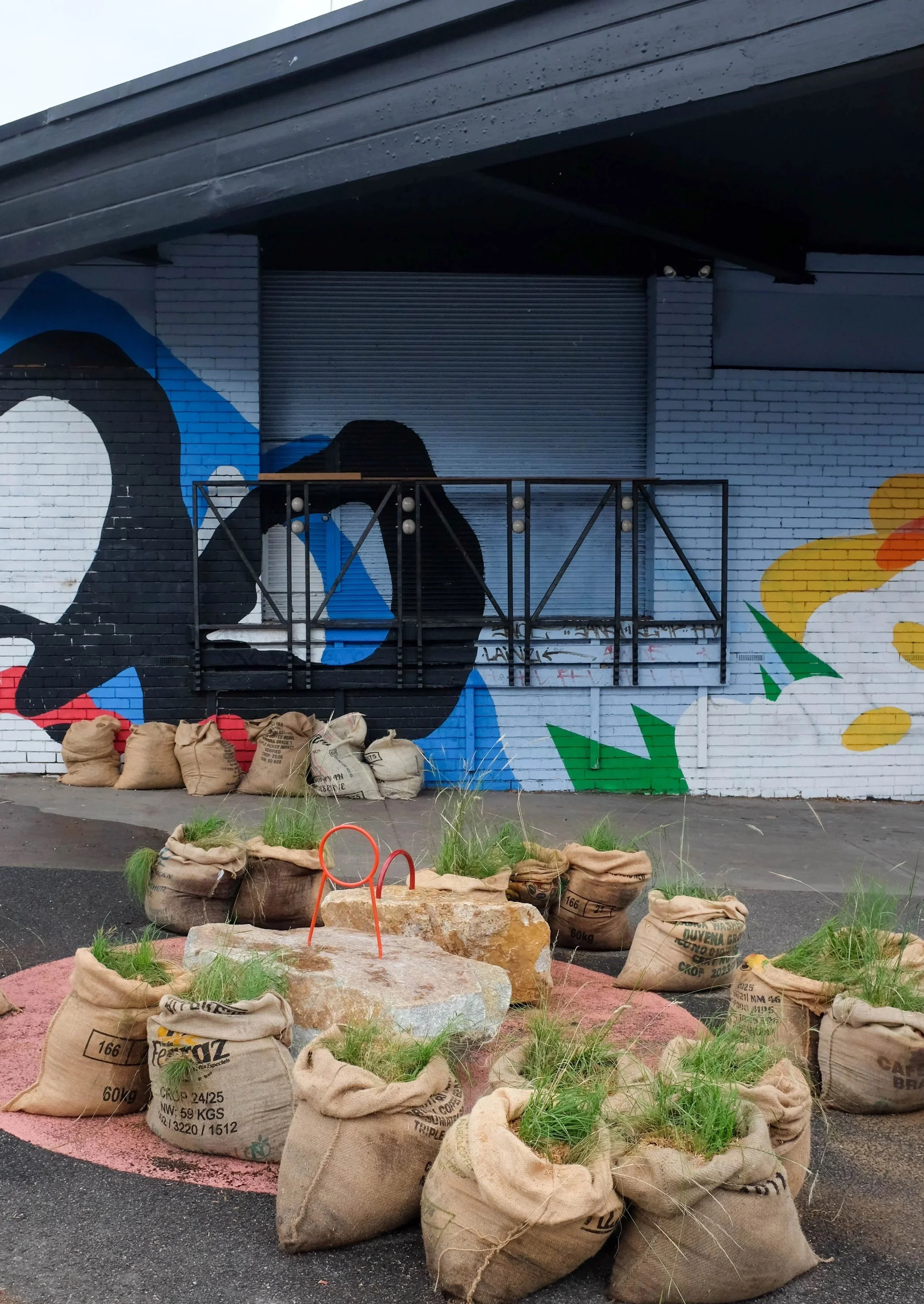 The circle of hessian sacks and granite in front of a colourful mural on a brick wall