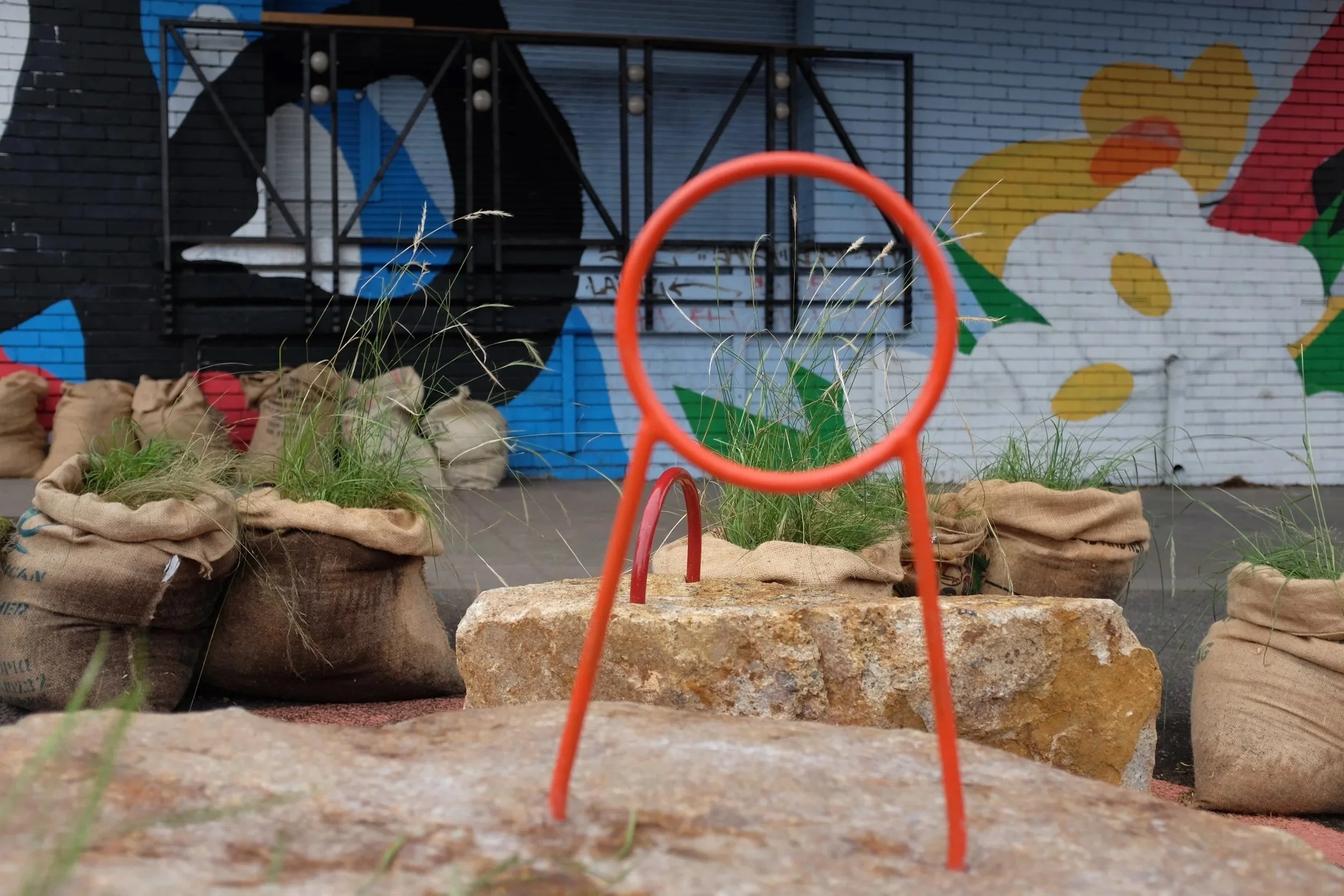 PARKing by Anita King: a red steel ring on granite blocks among grass-filled hessian sacks, in front of a painted mural