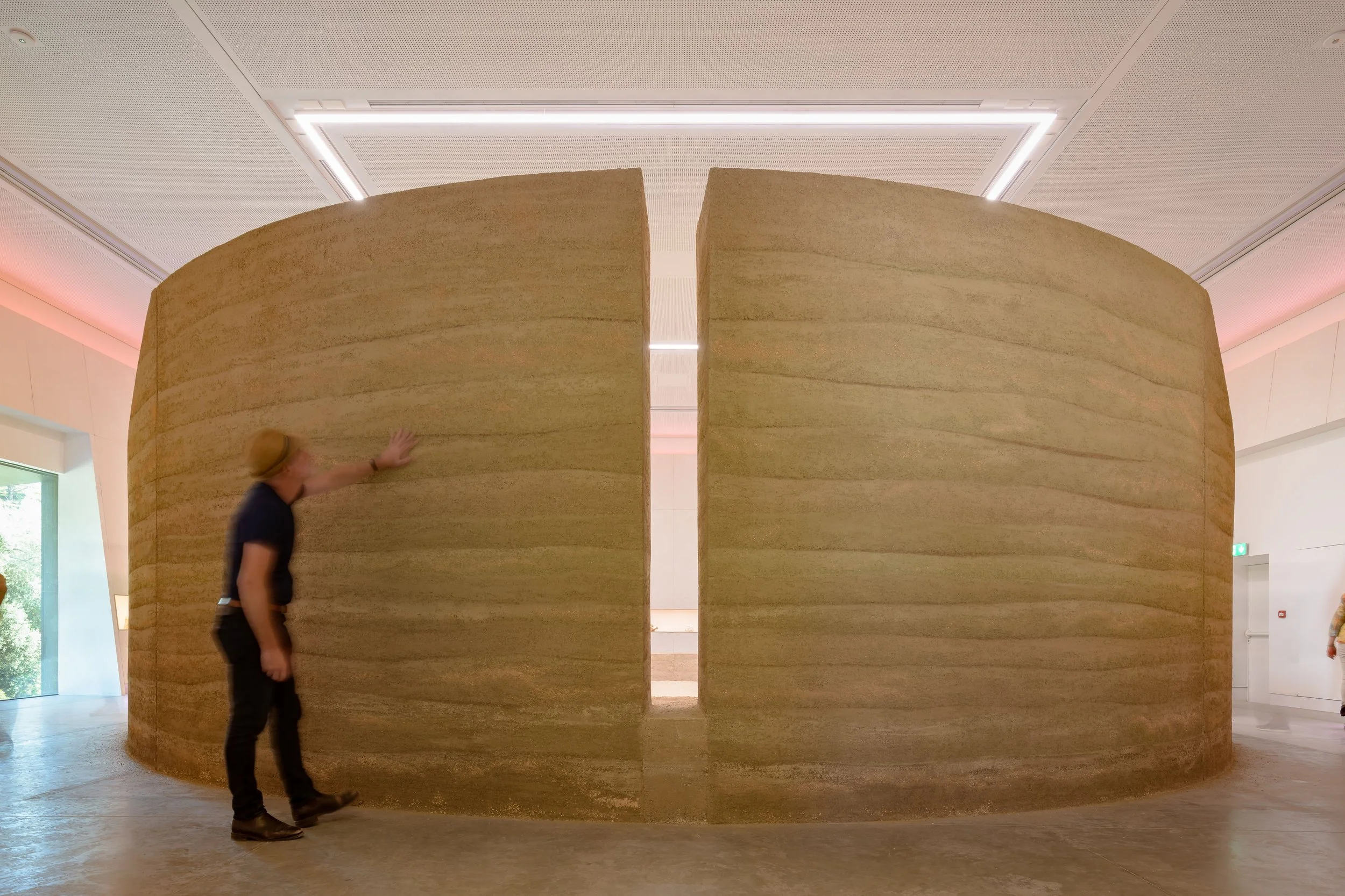 A visitor touching the monumental rammed earth wall, split by a narrow vertical opening