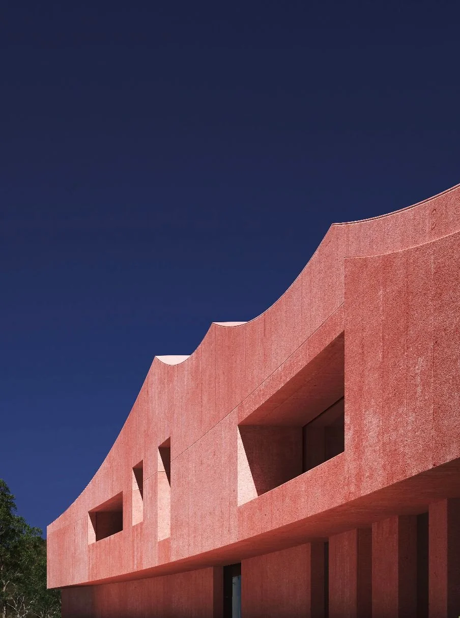 Curved red concrete facade against a deep blue evening sky