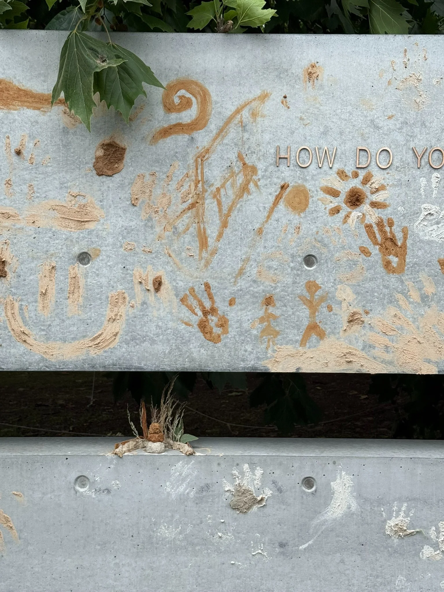 Close-up of ochre drawings, handprints and a smiley face on the concrete wall