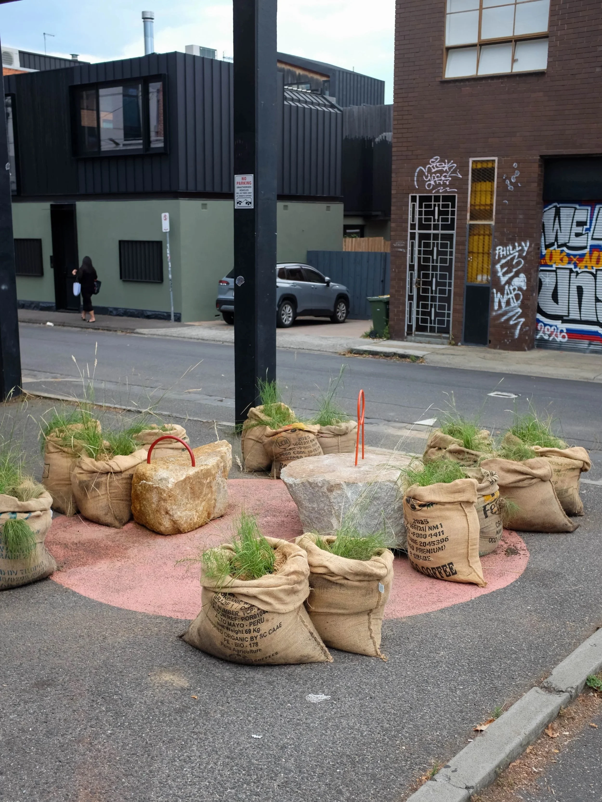 PARKing from across the street, a circle of grass-filled hessian sacks on a pink-painted parking space