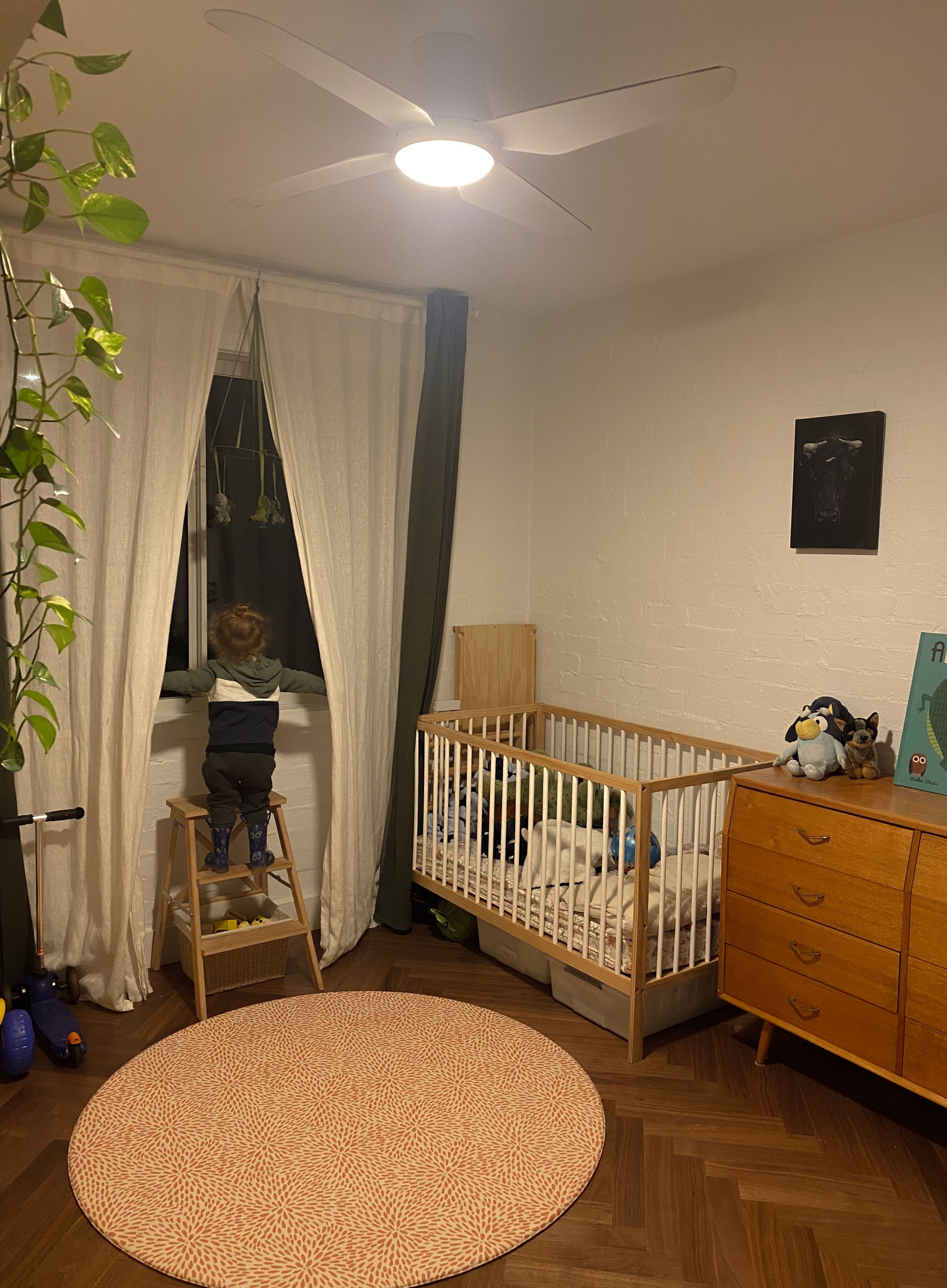 Bedroom set up as a nursery with a timber cot, sheer curtains and a round woven rug
