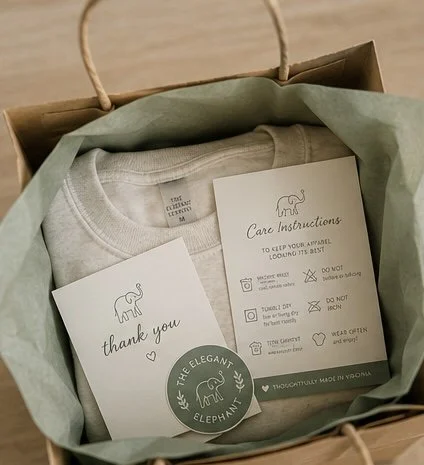 Care instructions, a thank you card, and a sticker with an elephant logo inside a gift box with tissue paper.