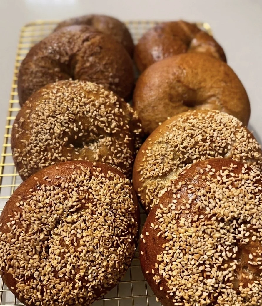 Assorted bagels with sesame seeds on top, placed on a wire rack.