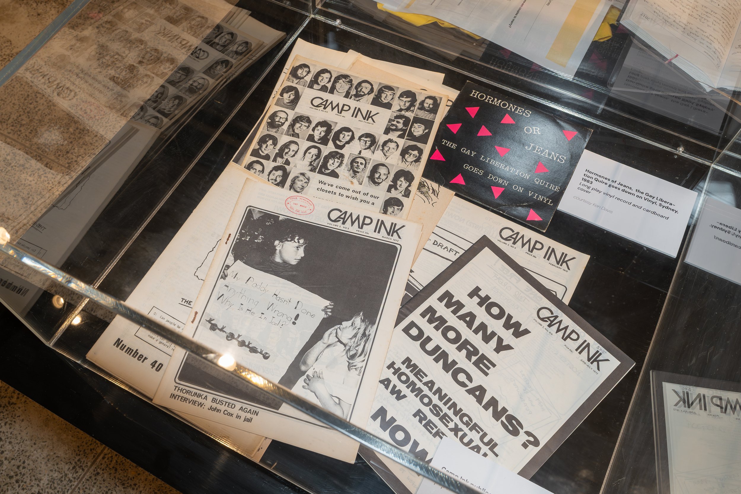 Display case with vintage copies of 'Camp Ink' magazine, featuring black-and-white headshots and articles about punk and alternative music and culture.