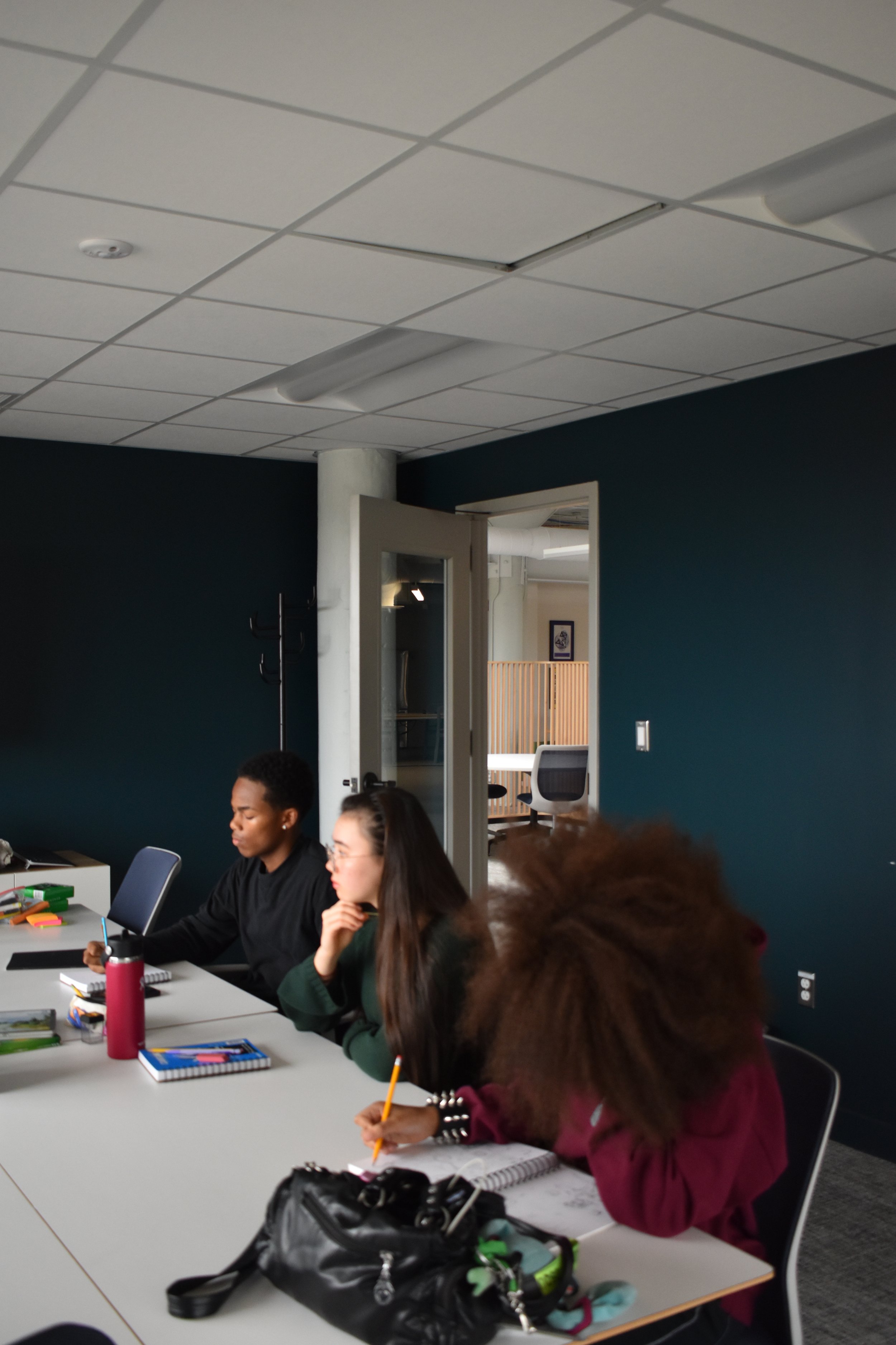 People sitting around a conference table in a modern office, with some taking notes, using laptops, and engaging in discussion.