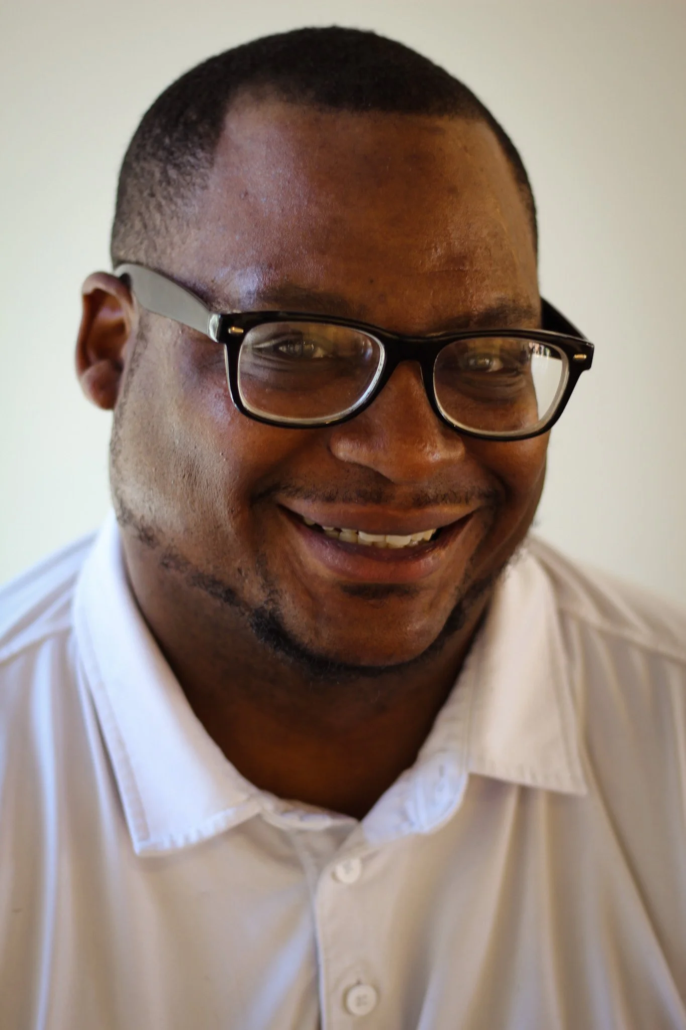A smiling man with short hair and glasses wearing a white button-up shirt.