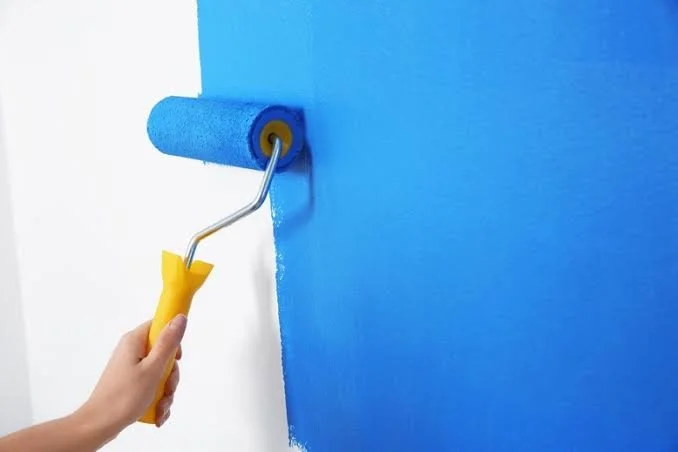 Person using a paint roller to paint a wall blue.