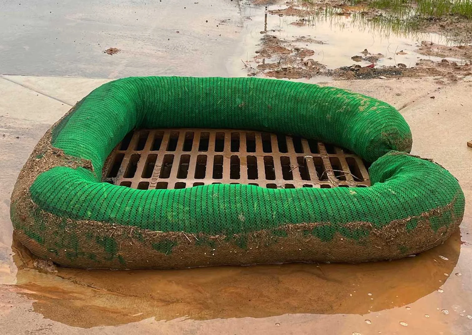 A green inflatable ring around a metal drain cover, with mud and water surrounding it.