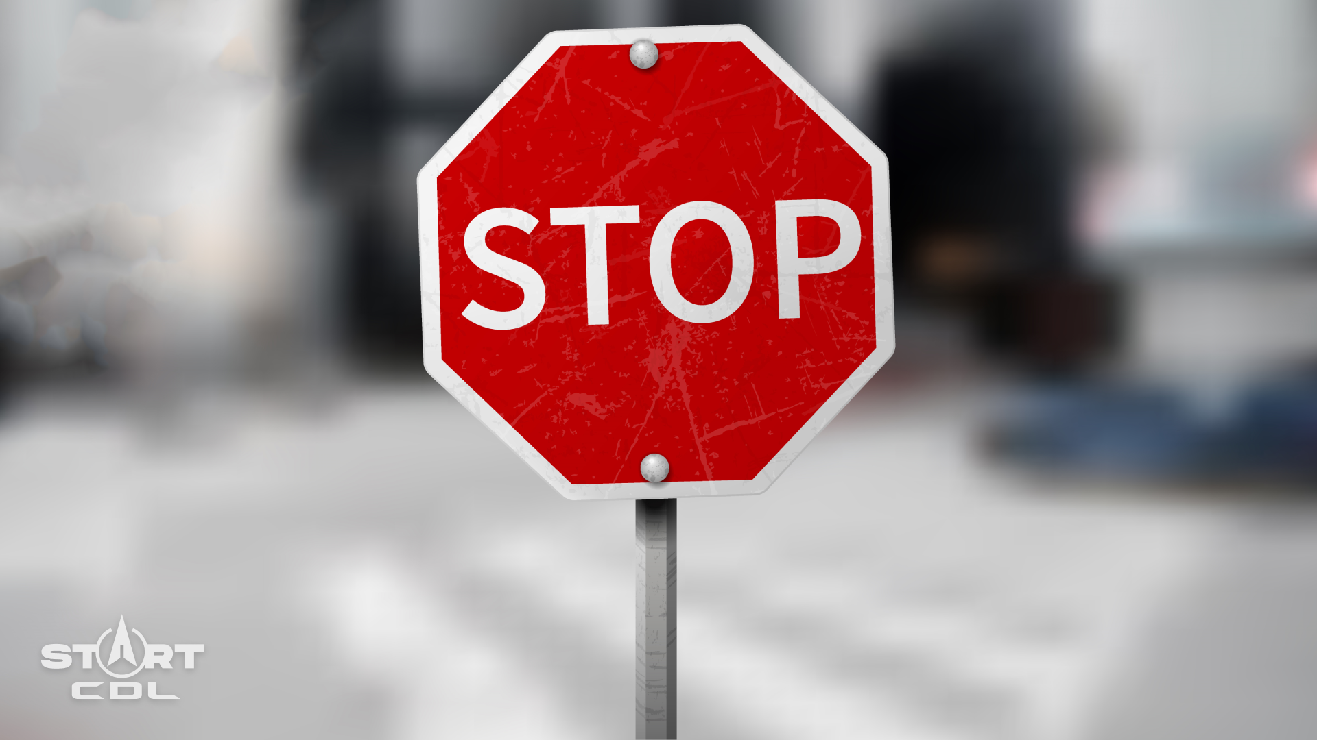 A red stop sign with a white border on a grey pole, with a blurred urban background.