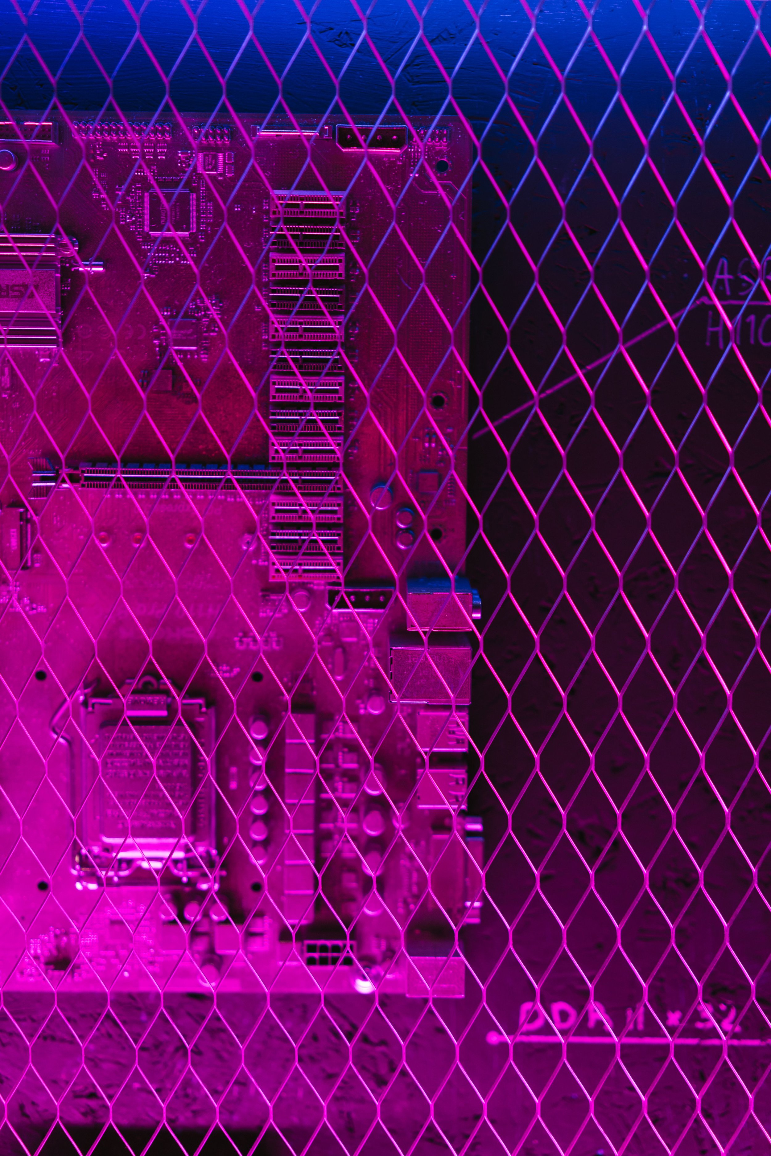 A computer motherboard behind a pink neon wire mesh in a dark setting.