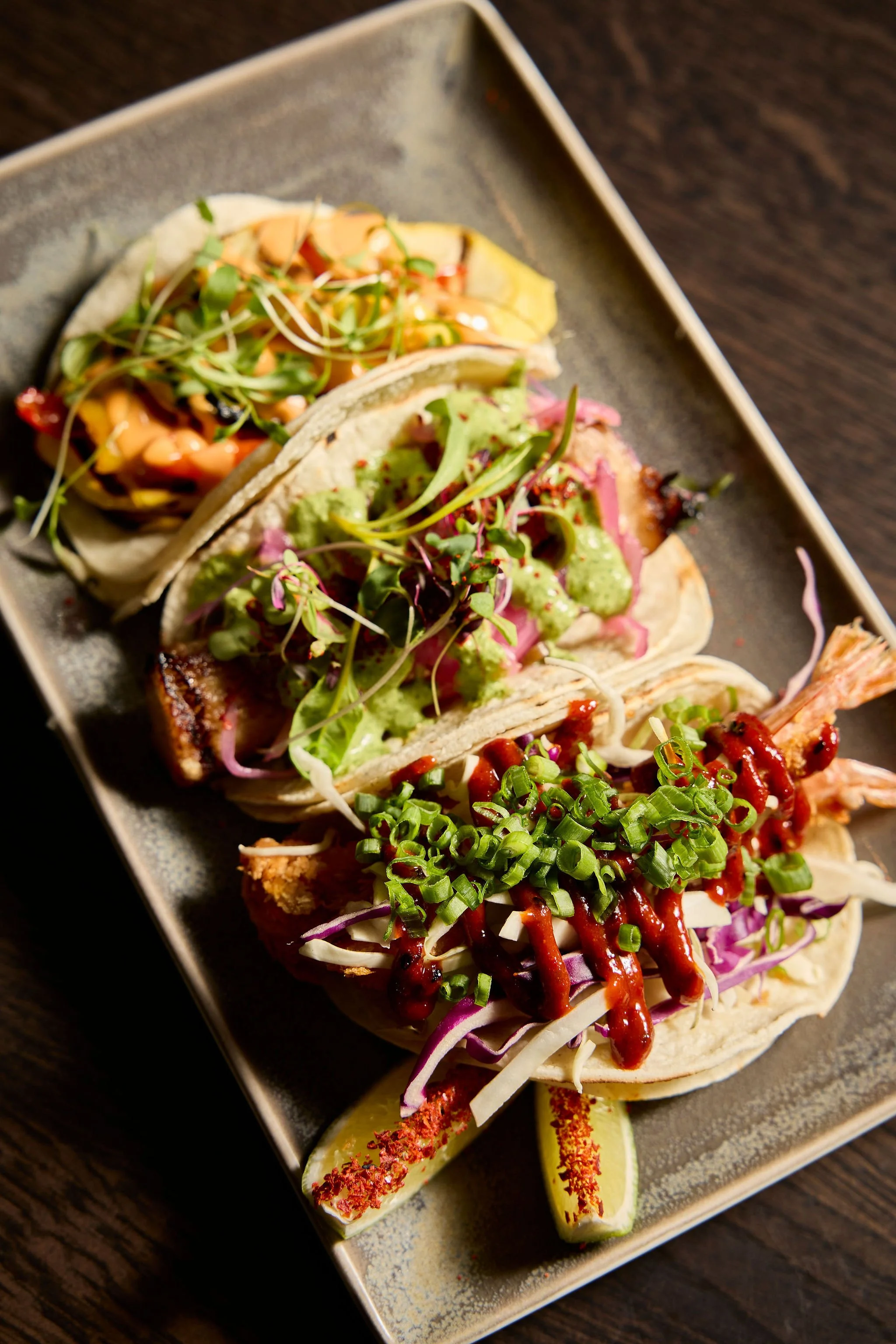 Close-up of assorted gourmet tacos topped with vegetables, microgreens, sauces, and green onions on a serving platter