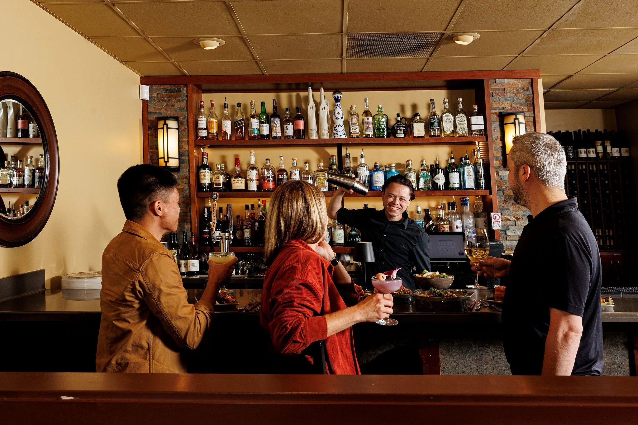 A group of four friends socializing and enjoying drinks at a bar or restaurant. One woman is serving drinks to the others, while they chat and have food.