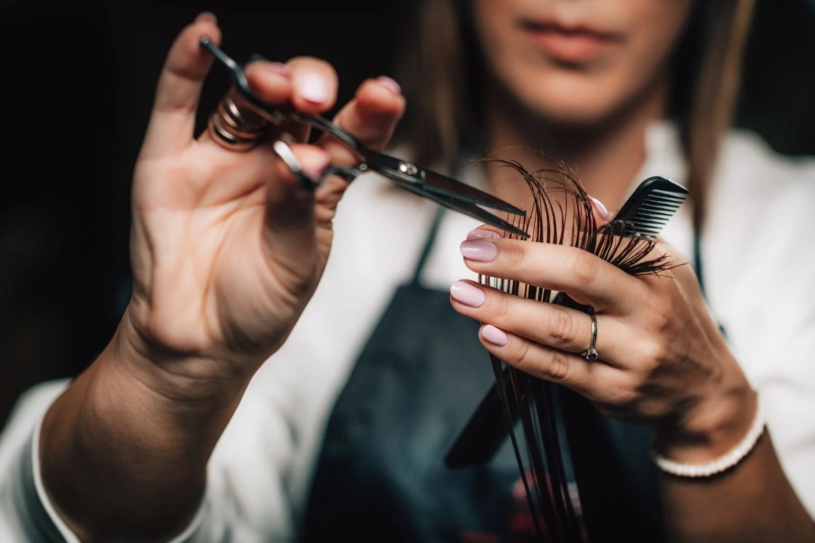A person getting a haircut and styling with scissors and a comb, holding hair pins or clips.