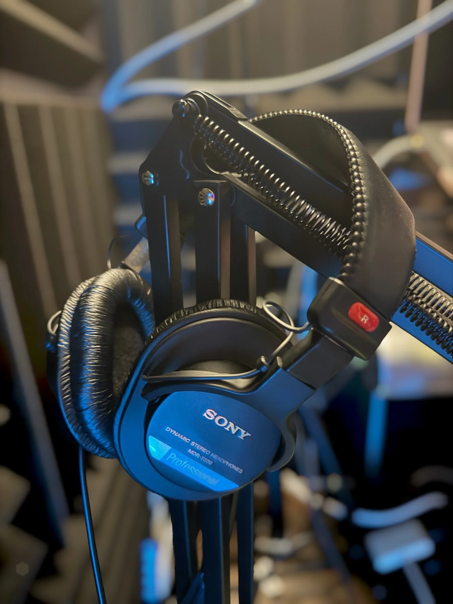 Close-up of black headphones hanging on a stand with cables in the background.