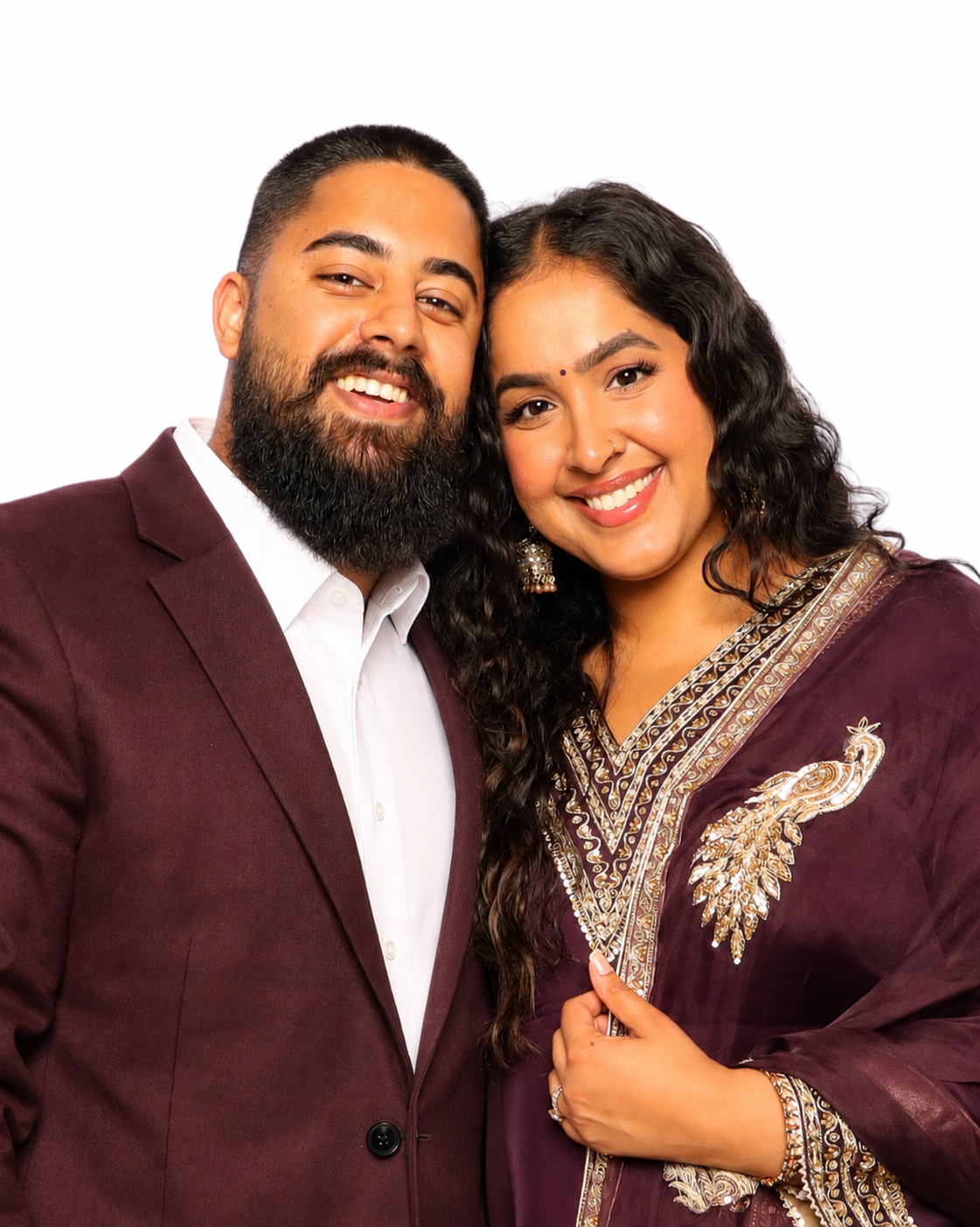 A happy couple with Indian ethnicity smiling closely together, dressed in formal attire, against a plain white background.
