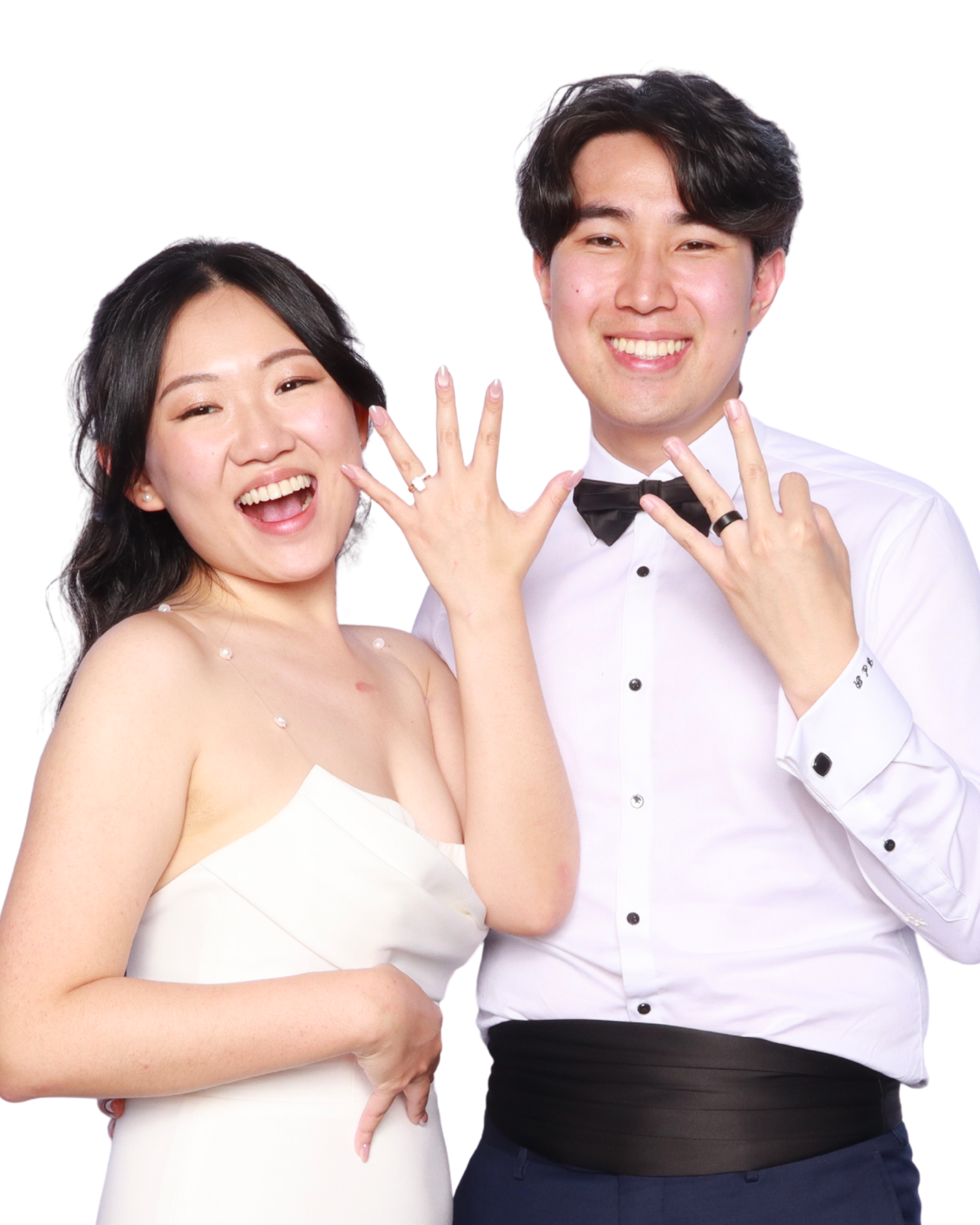 Happy couple celebrating their wedding, showing rings on fingers, dressed in formal attire, white background.